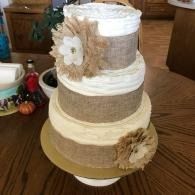 Three-tier burlap and white rustic cake with flower decorations on a wooden table