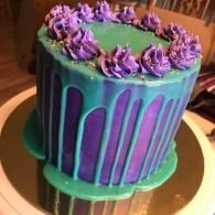 Purple and teal frosted cake with drip icing and piped rosettes on a cake stand