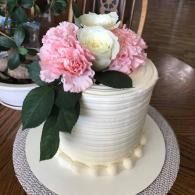 White frosted cake with pink and white flowers on top, on a woven placemat on a table