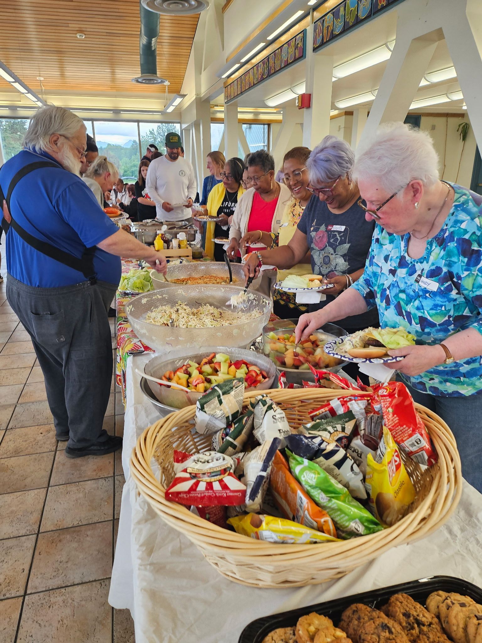 People at a buffet table, selecting food. Salad, snacks, and cookies are visible.