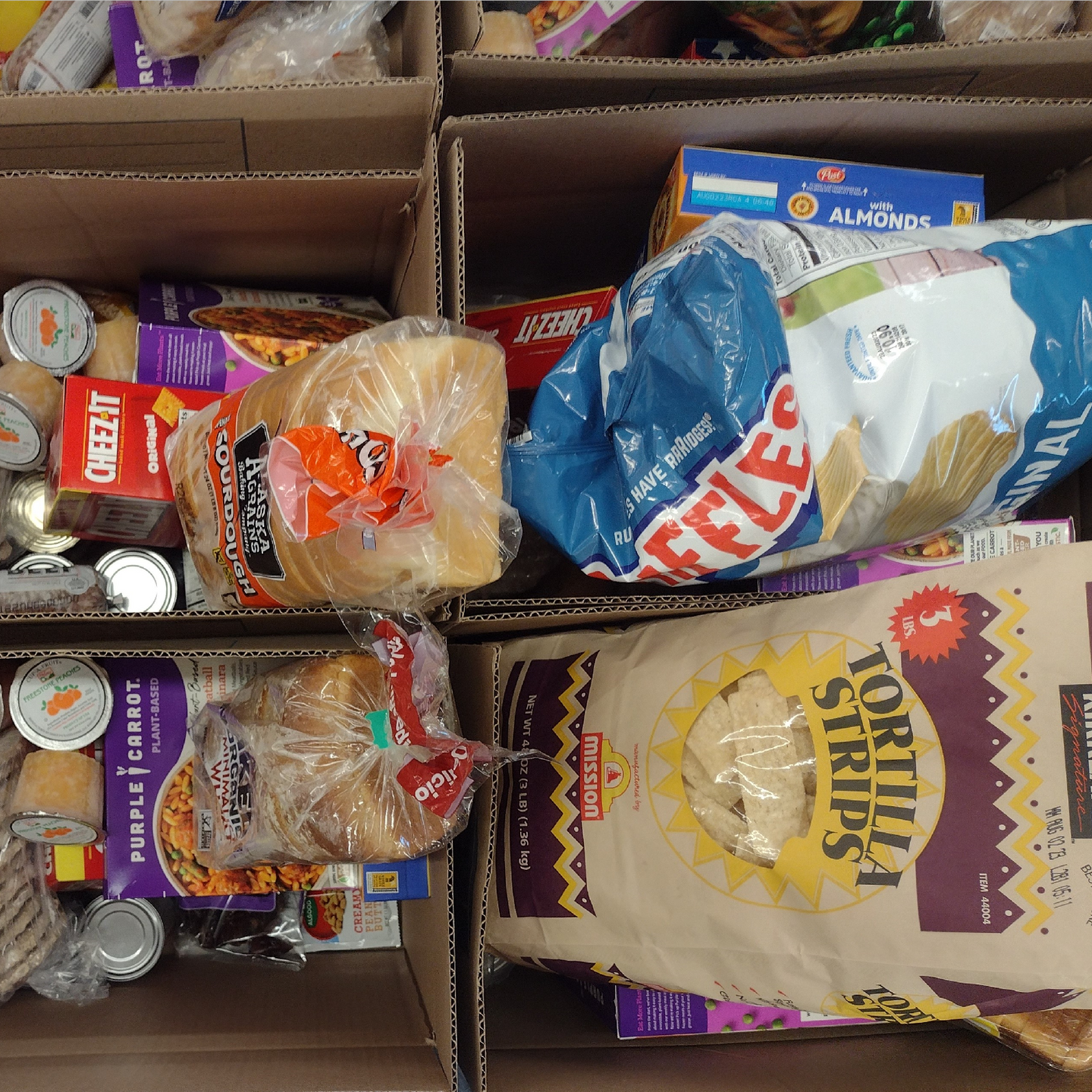 Cardboard boxes filled with packaged food items, including bread, snacks, and canned goods, likely for donation.