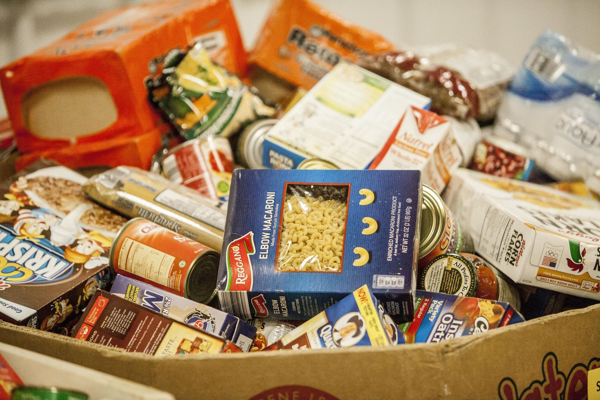 Boxes of food stacked on a table, ready for distribution. Other boxes and bags of food on the floor.