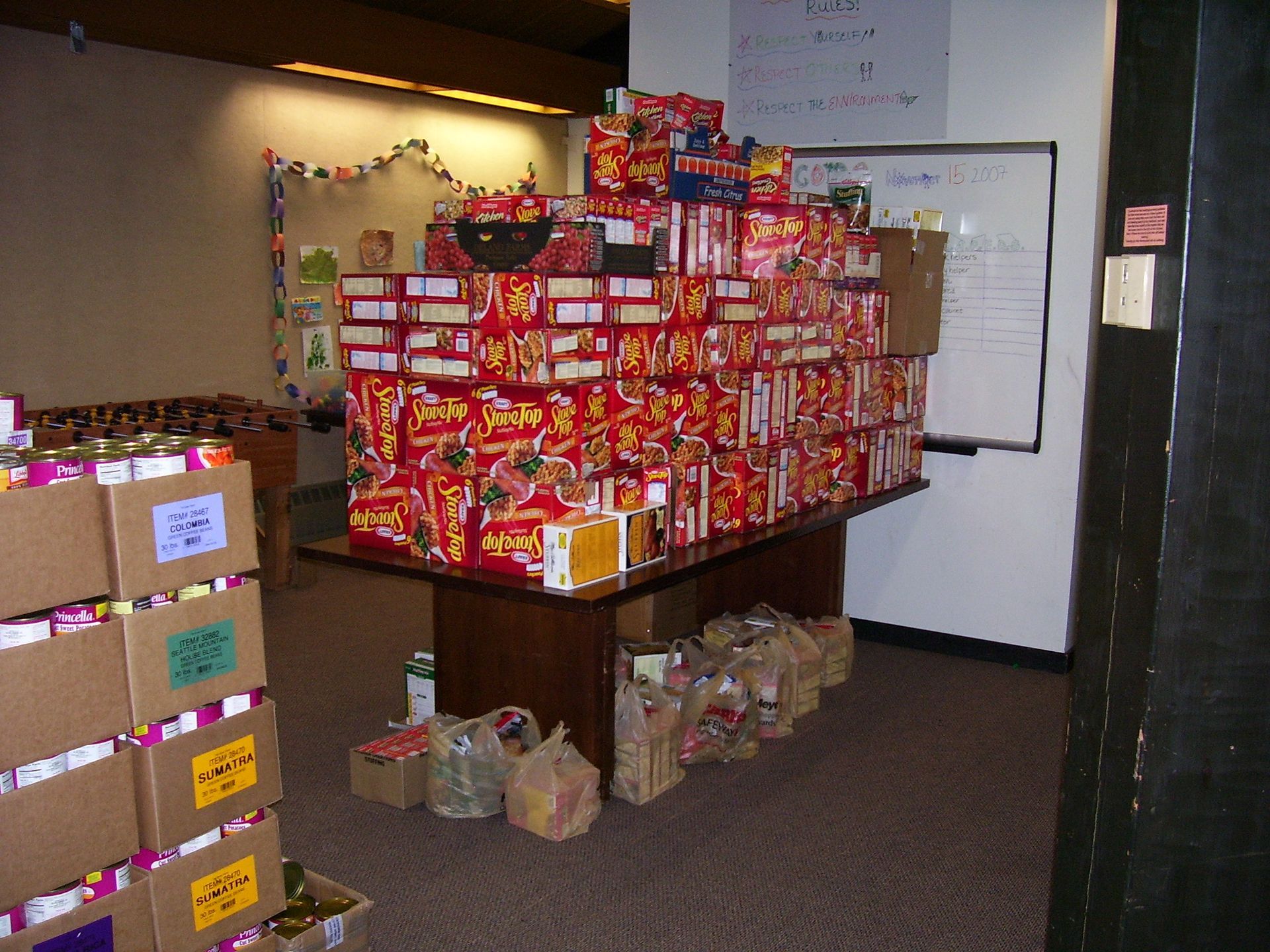 Boxes of food stacked on a table, ready for distribution. Other boxes and bags of food on the floor.