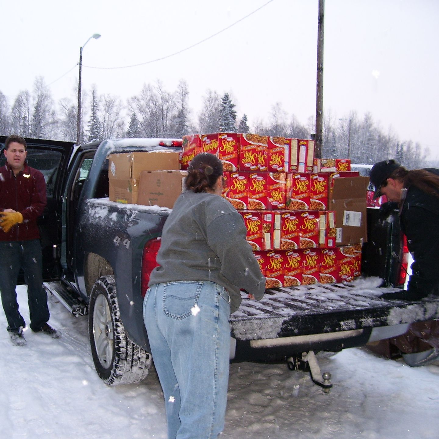 People loading boxes of food into a pickup truck in the snow.