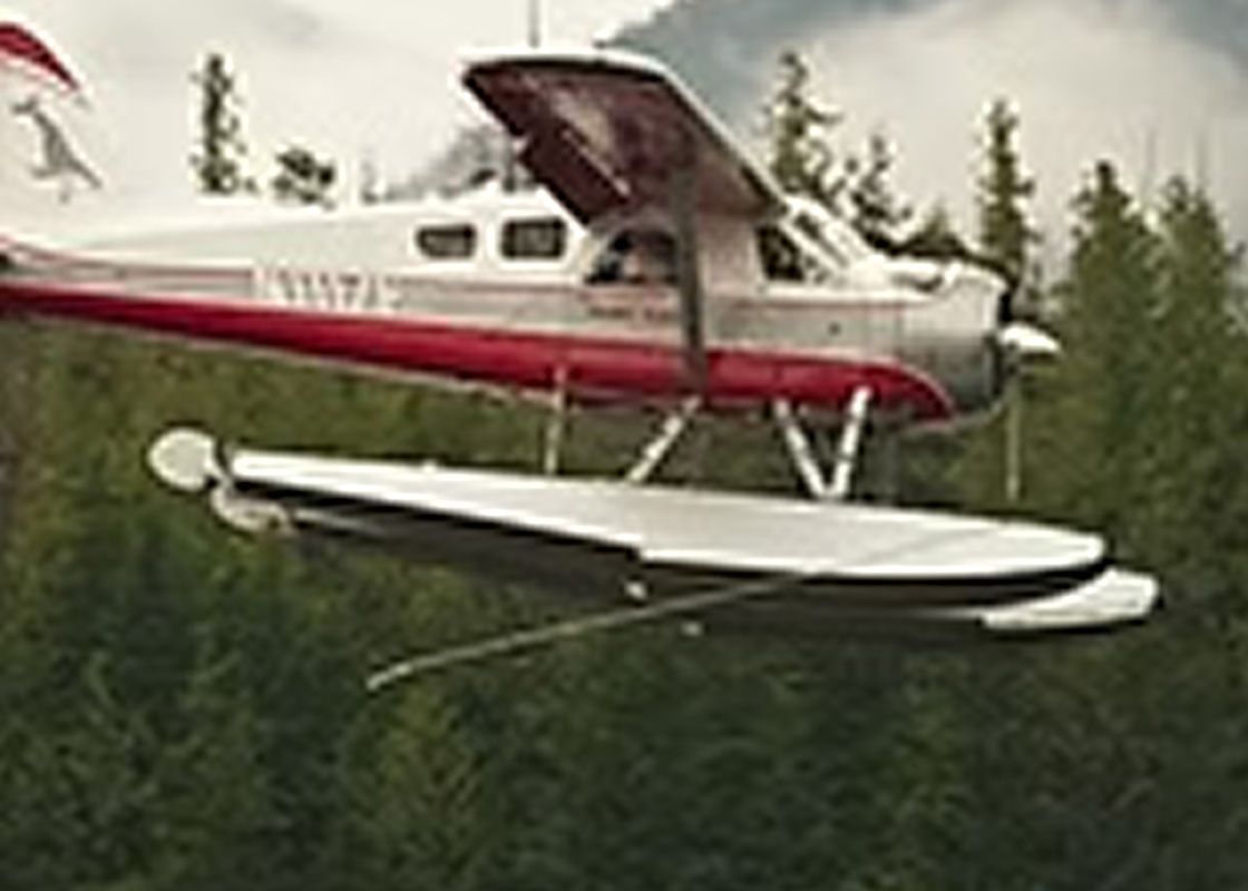 Seaplane with red and white fuselage flies over green trees.