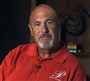 Man with shaved head in red polo shirt, smiling, indoors.