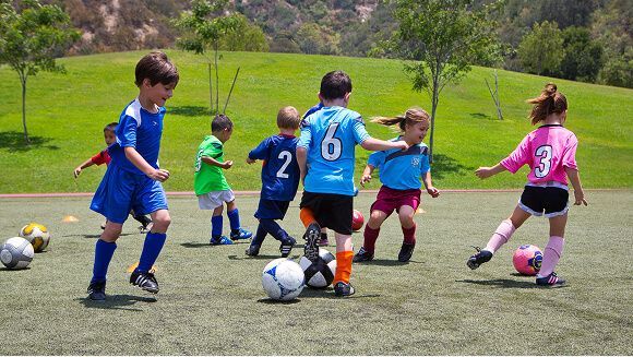 Children in colorful jerseys practice soccer drills on a grassy field.