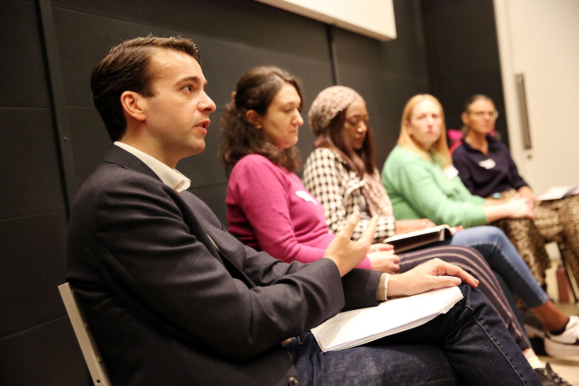 A group of people are sitting in a row with notebooks in their lap.