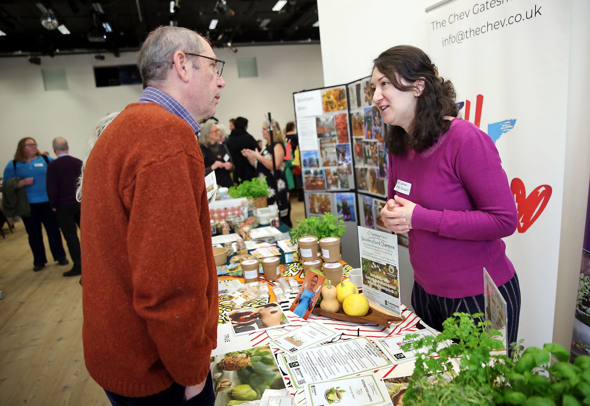 A woman in a purple sweater is talking to a man in an orange sweater