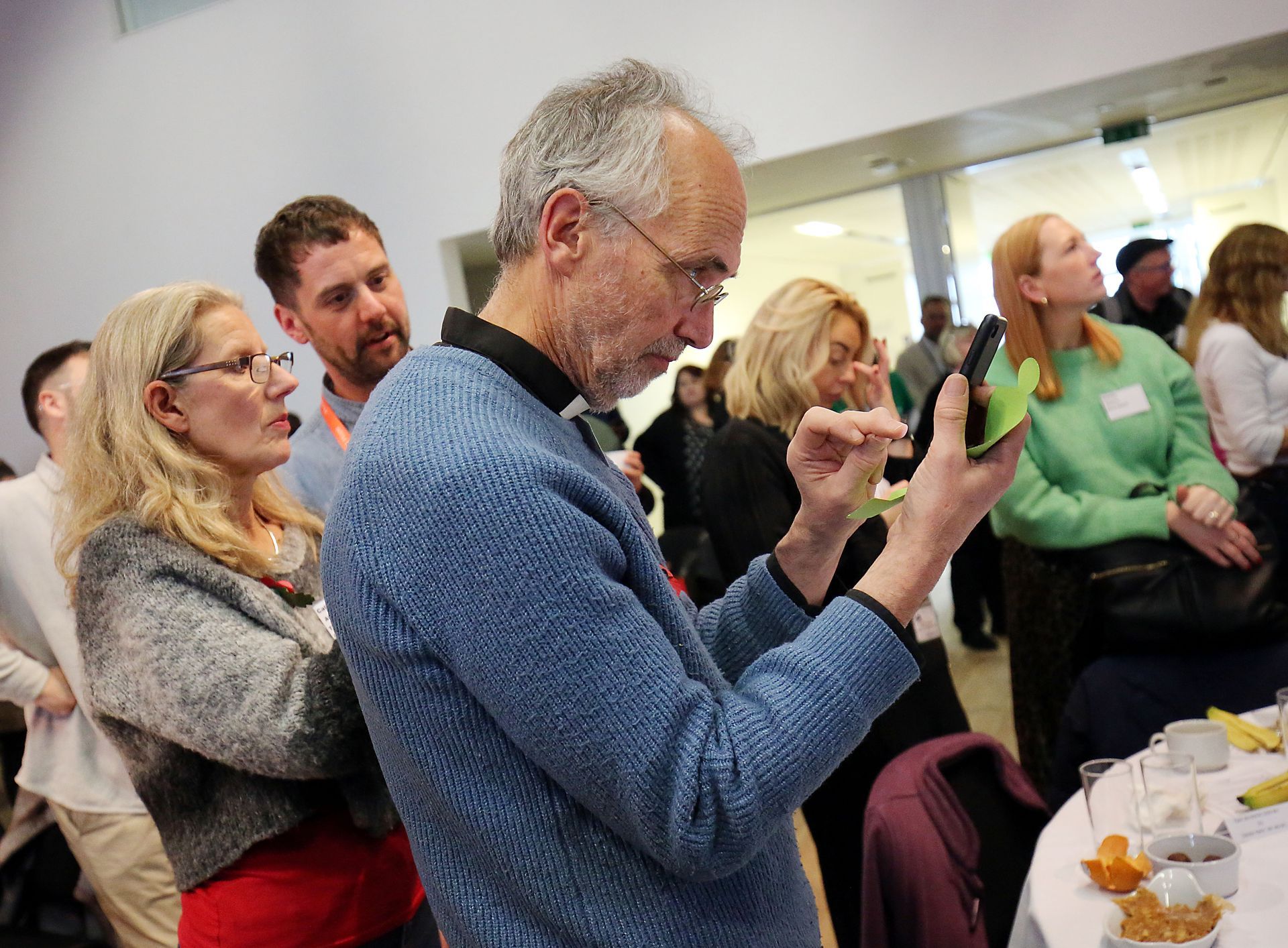 A man in a blue sweater is taking a picture of a group of people.