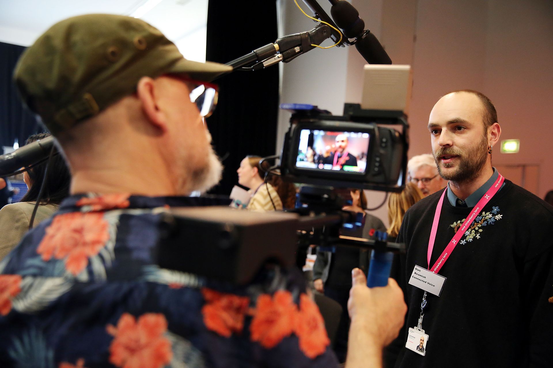 A man in a floral shirt is being interviewed by a cameraman