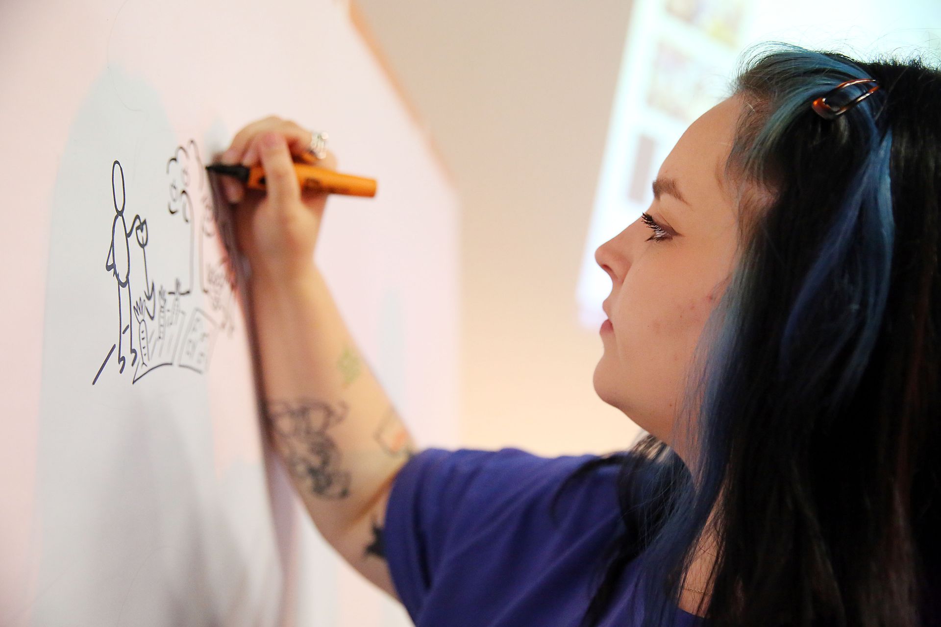 A woman with blue hair is writing on a white board with a marker.