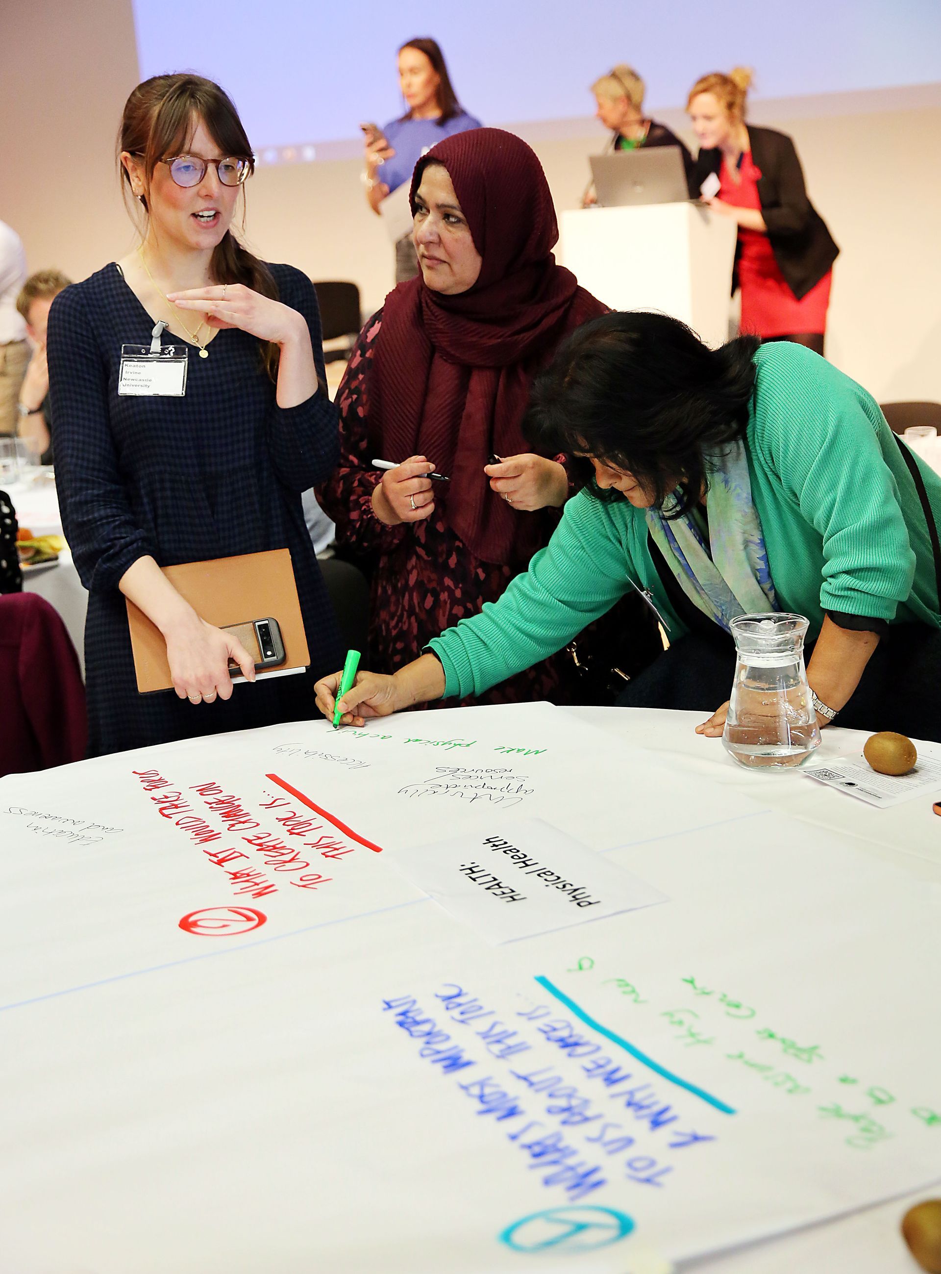 A group of women are writing on a large piece of paper