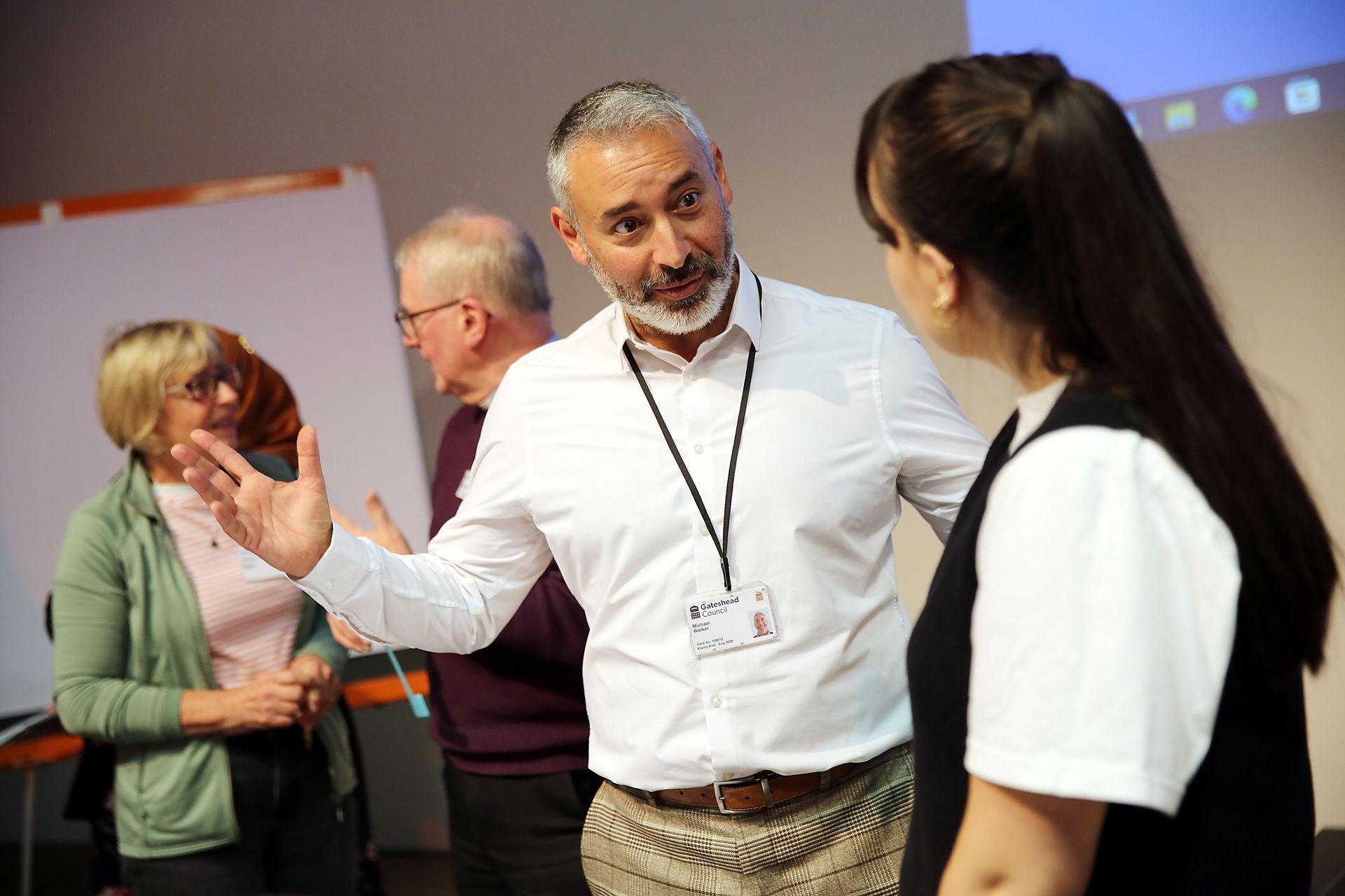 A man with a beard is talking to a woman in a room.