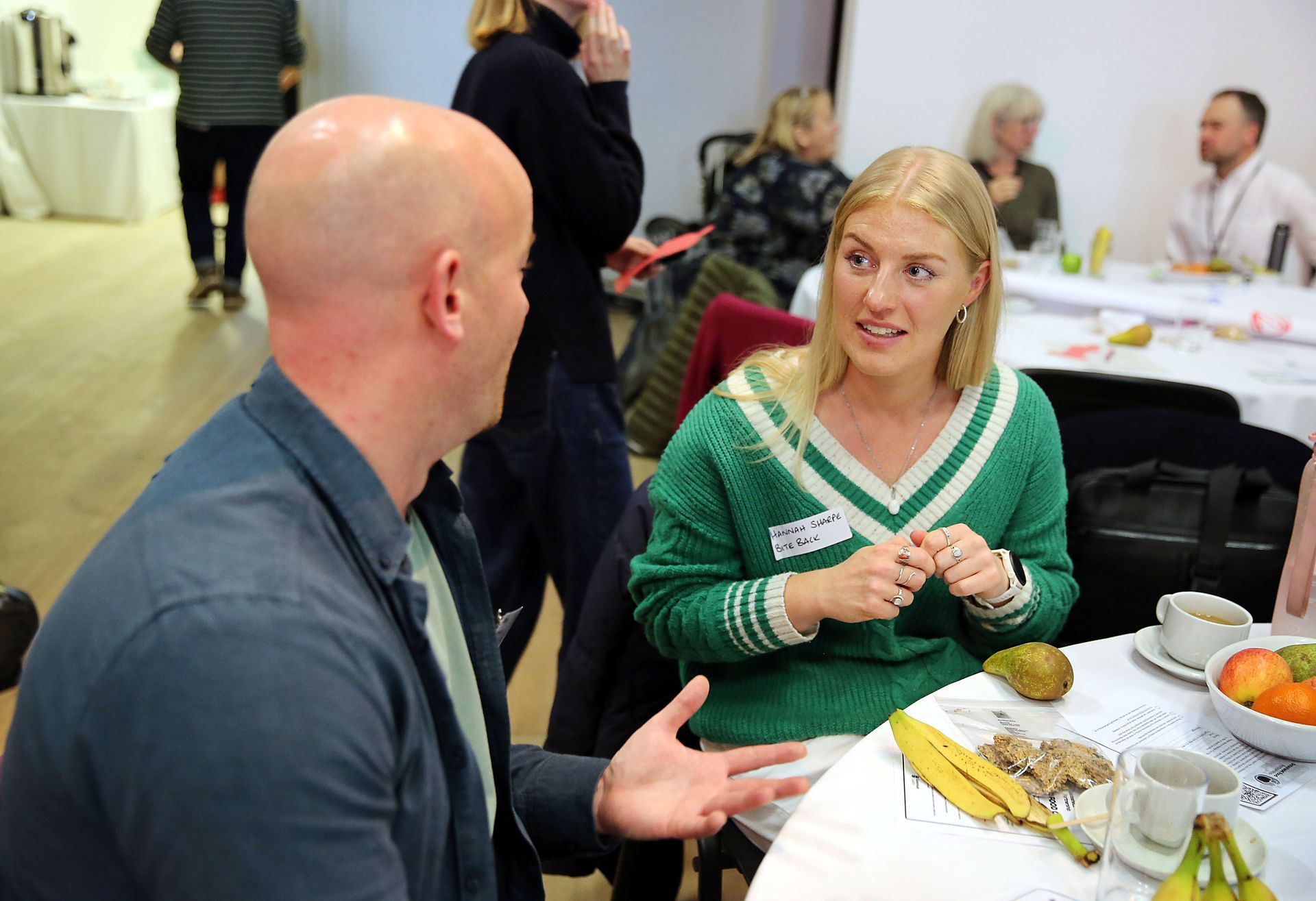 A man and a woman are sitting at a table talking to each other.