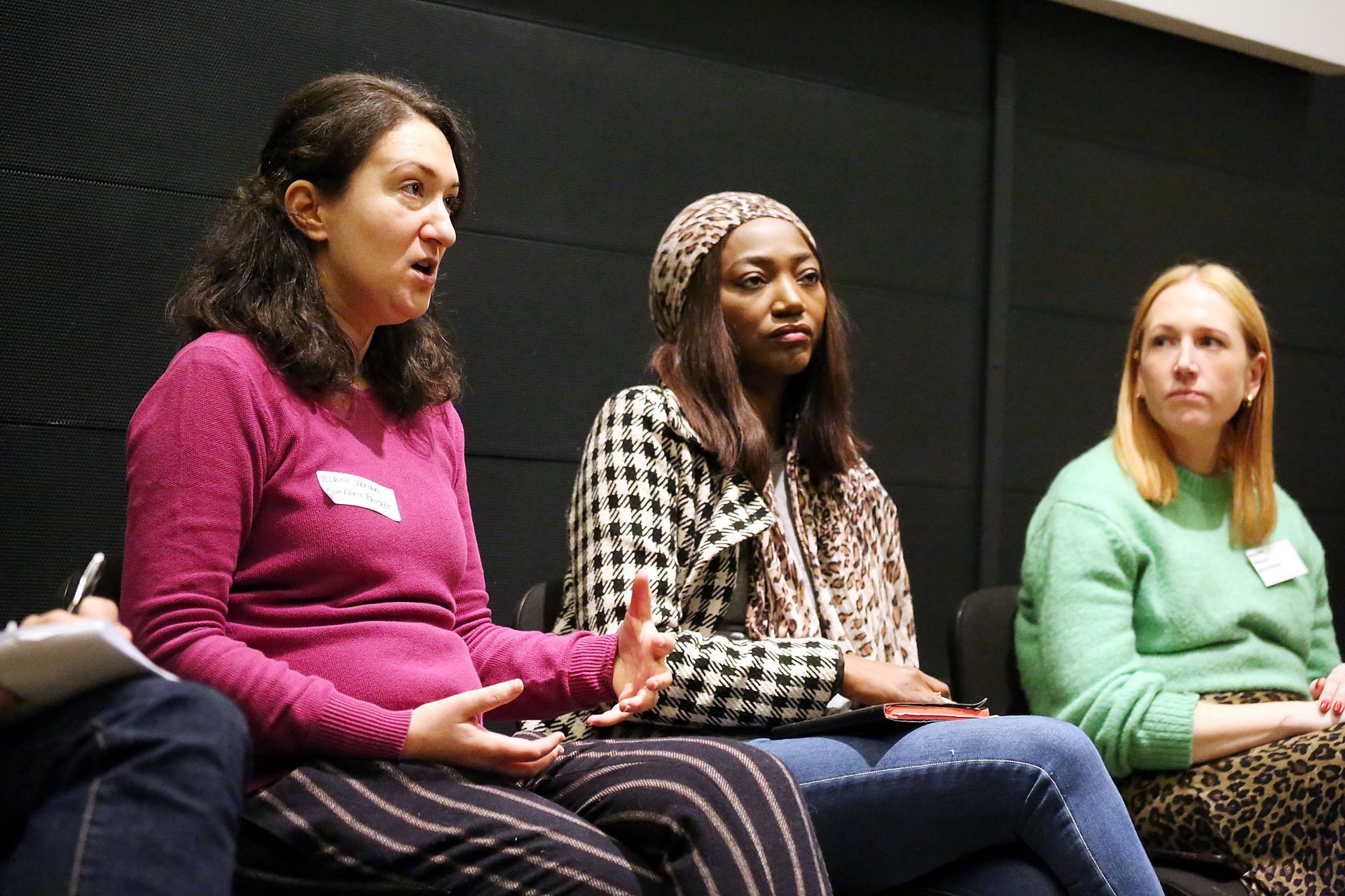 Three women are sitting on a couch talking to each other.