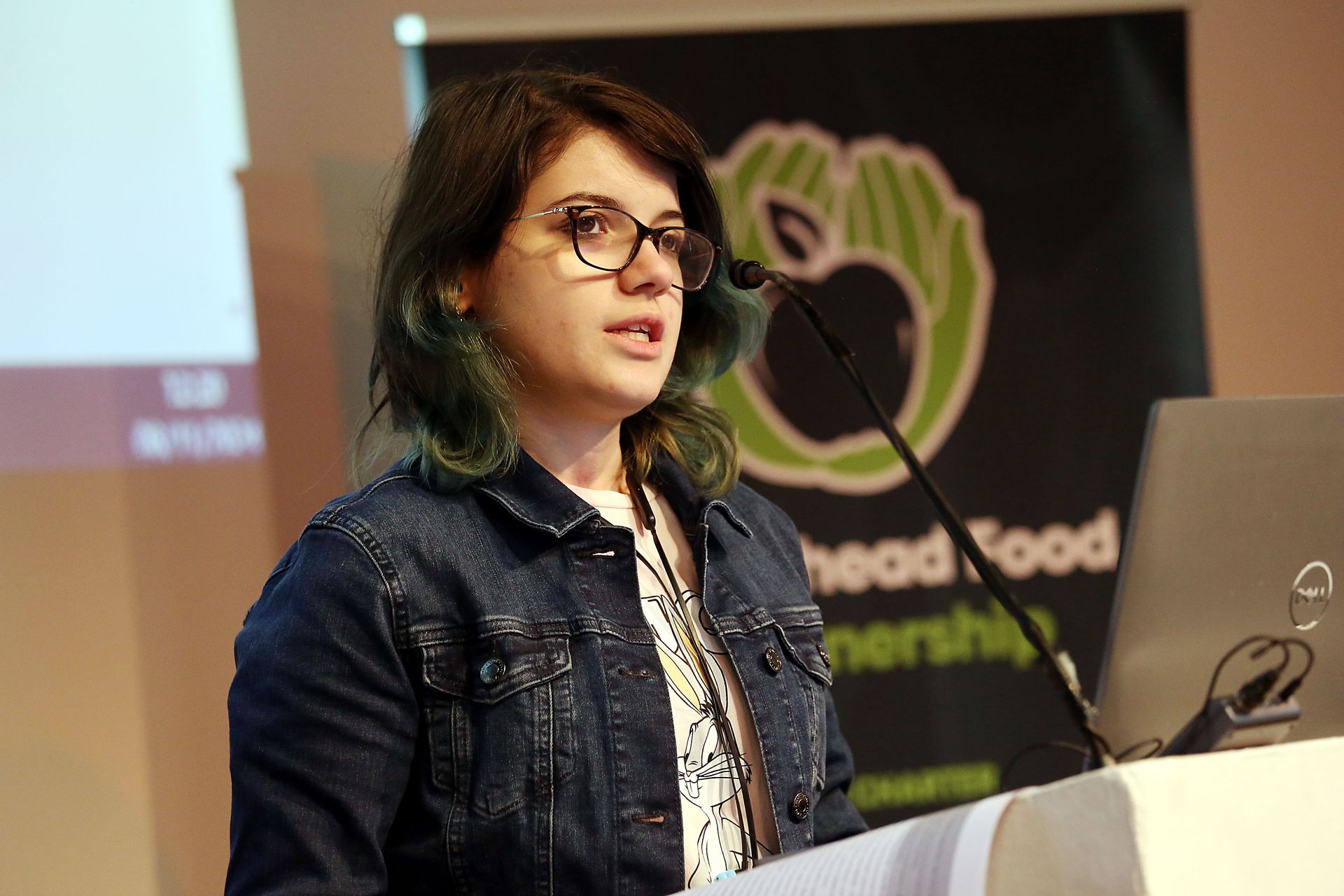 A woman is standing at a podium speaking into a microphone.