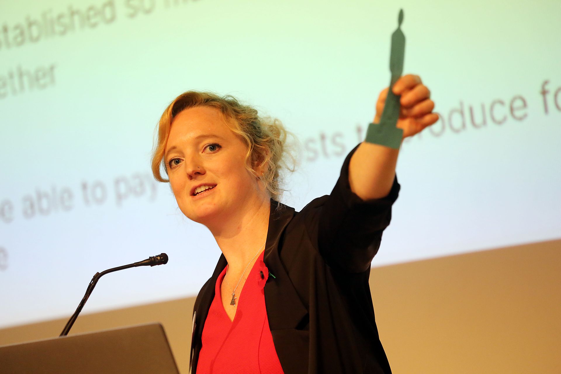 A woman stands at a podium holding up a green object