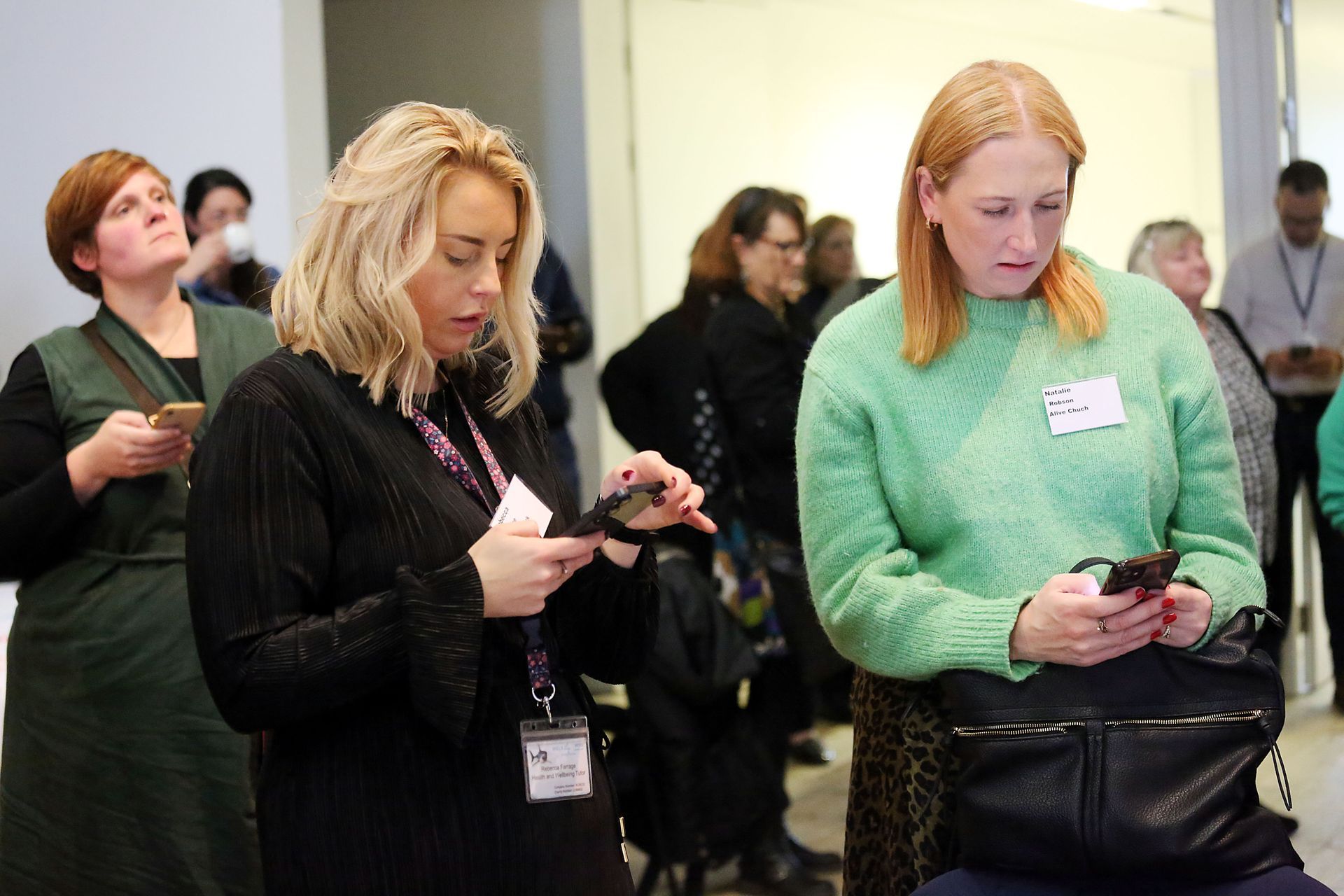 Two women are standing next to each other looking at their phones.