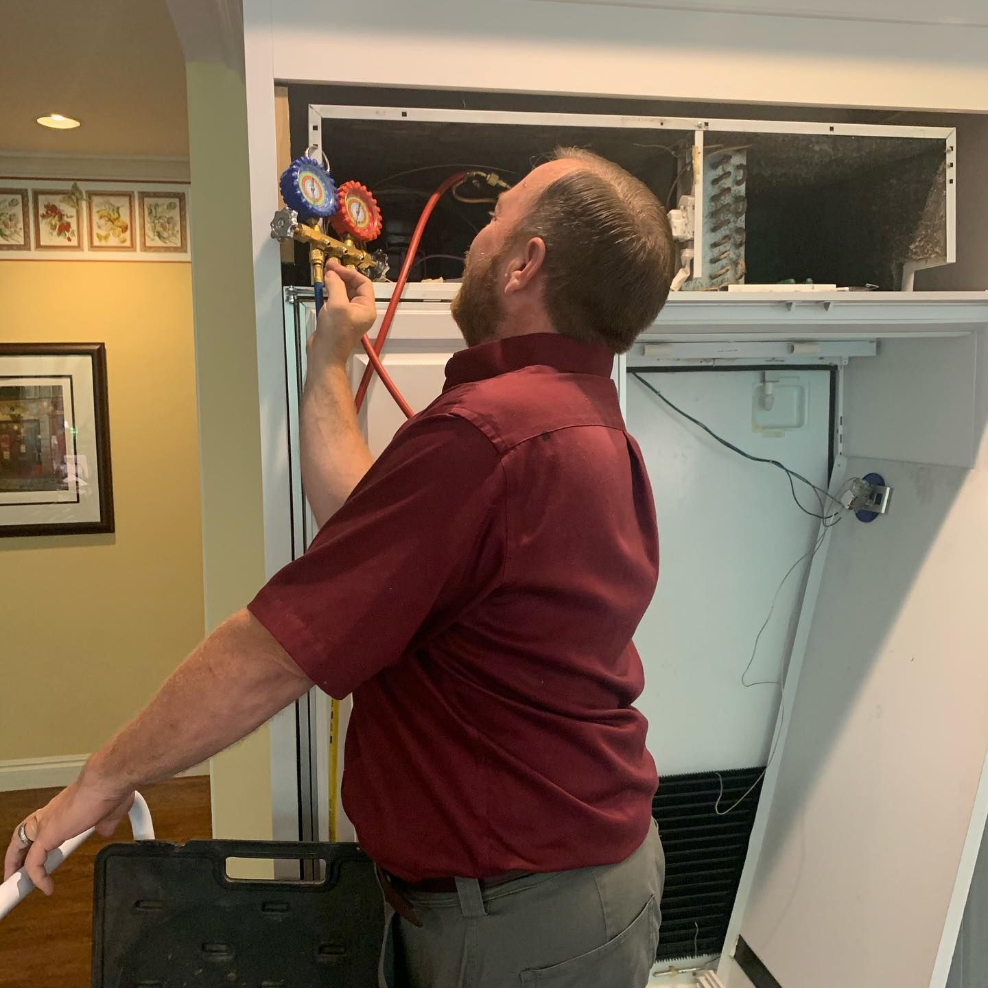 a man in a red shirt is working on a refrigerator .