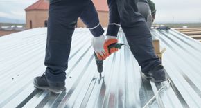 a man is using a drill to drill a hole in a metal roof .