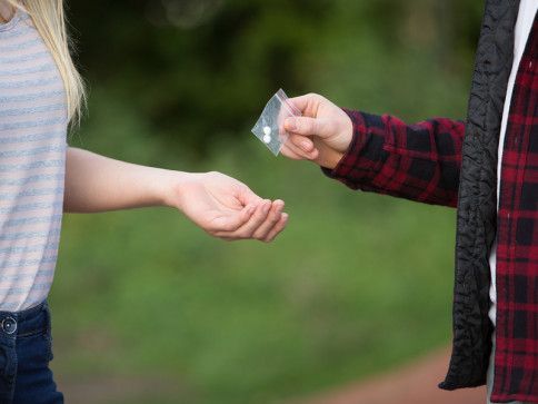 Person handing a small bag with white object to another person's open hand. Blurred outdoor setting.