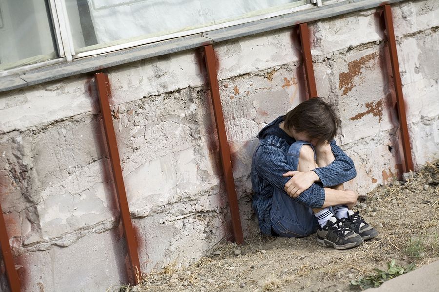 Child huddled against a concrete wall, head down, knees drawn up.