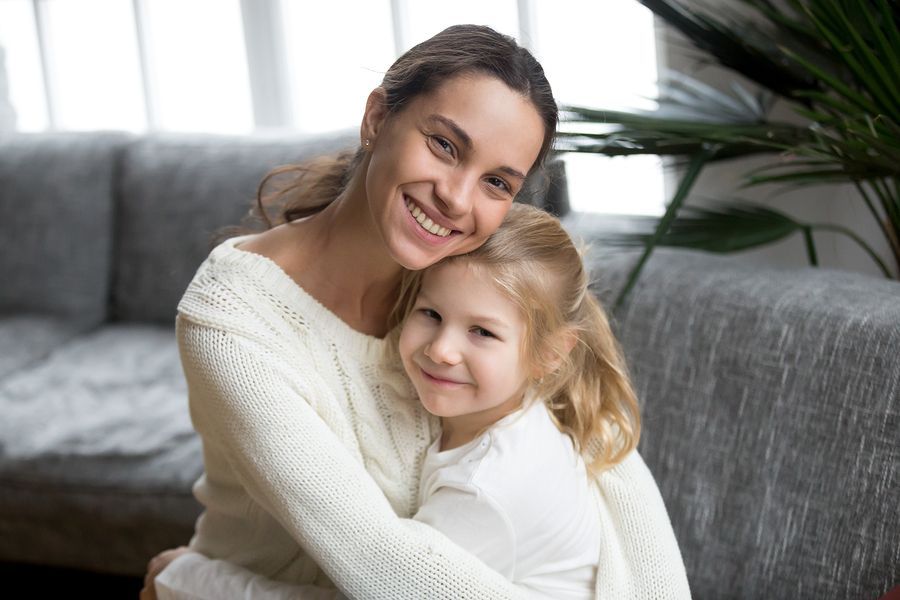 Woman hugging child, both smiling, sitting on a couch.