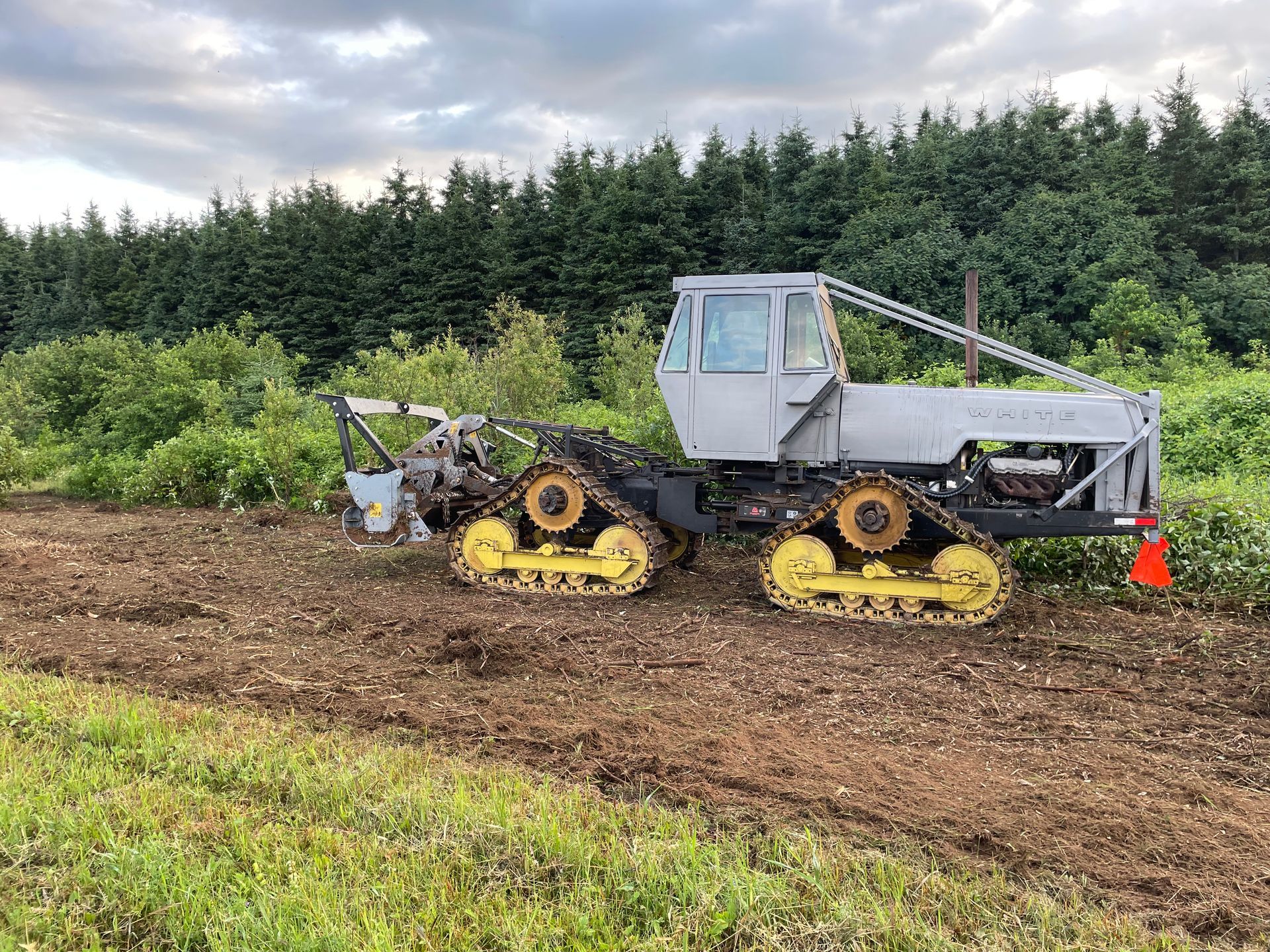 Un tracteur avec des chenilles jaunes traverse un champ.