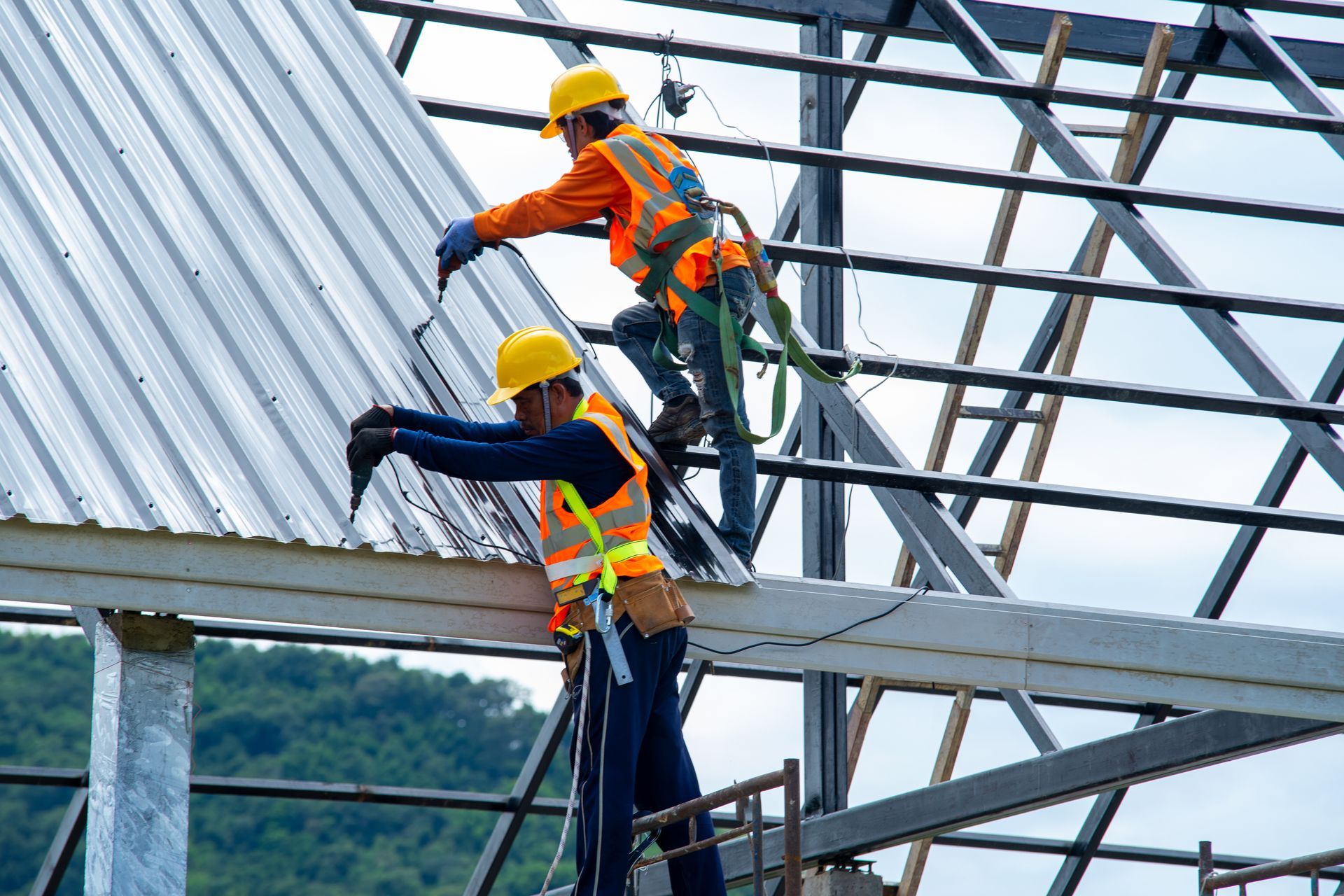 Crew installing metal roof panels on steel-framed building structure.