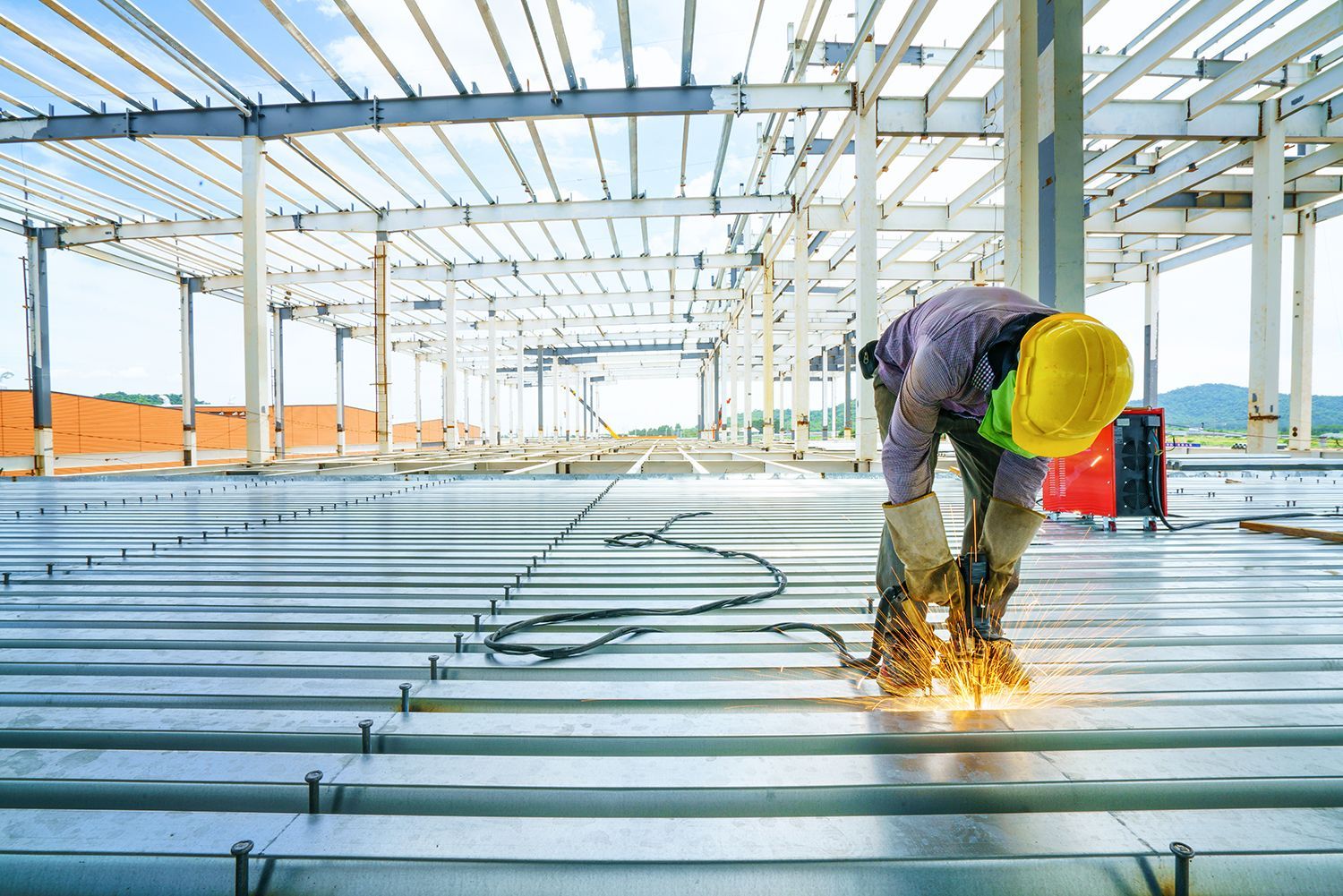 Construction worker welding steel panels during metal building installation.