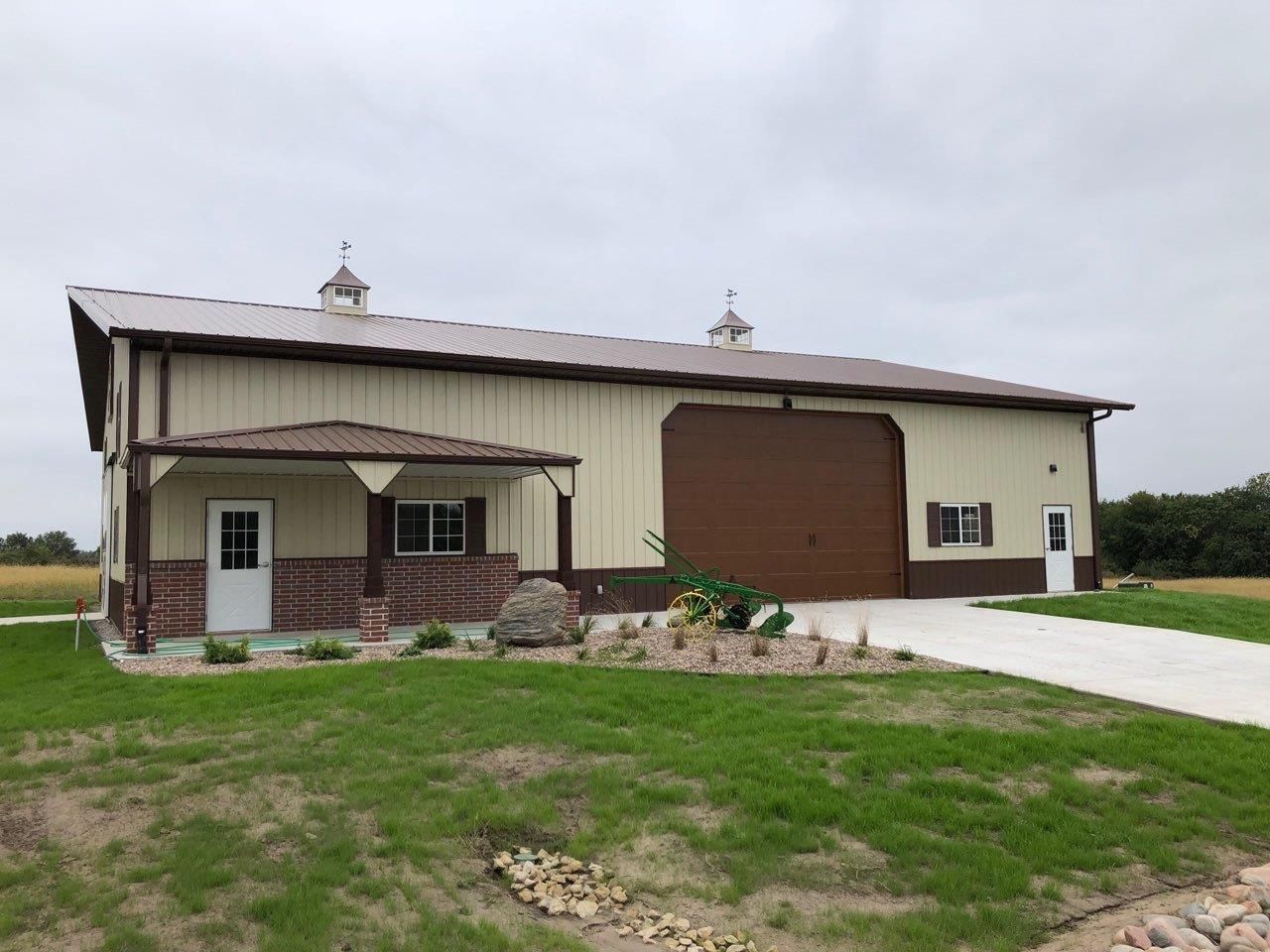 Tan and brown metal building with porch, garage door, and weathervanes.