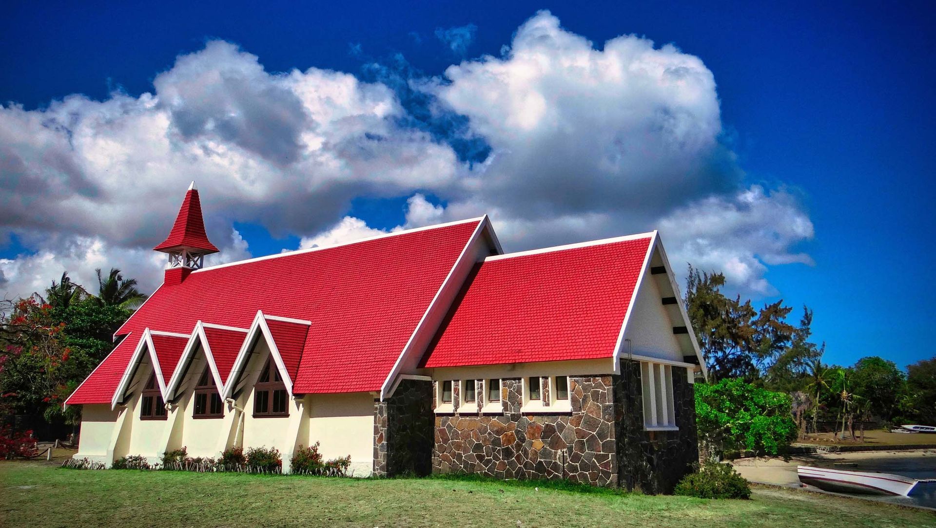 Church with red roof against blue sky and puffy white clouds.
