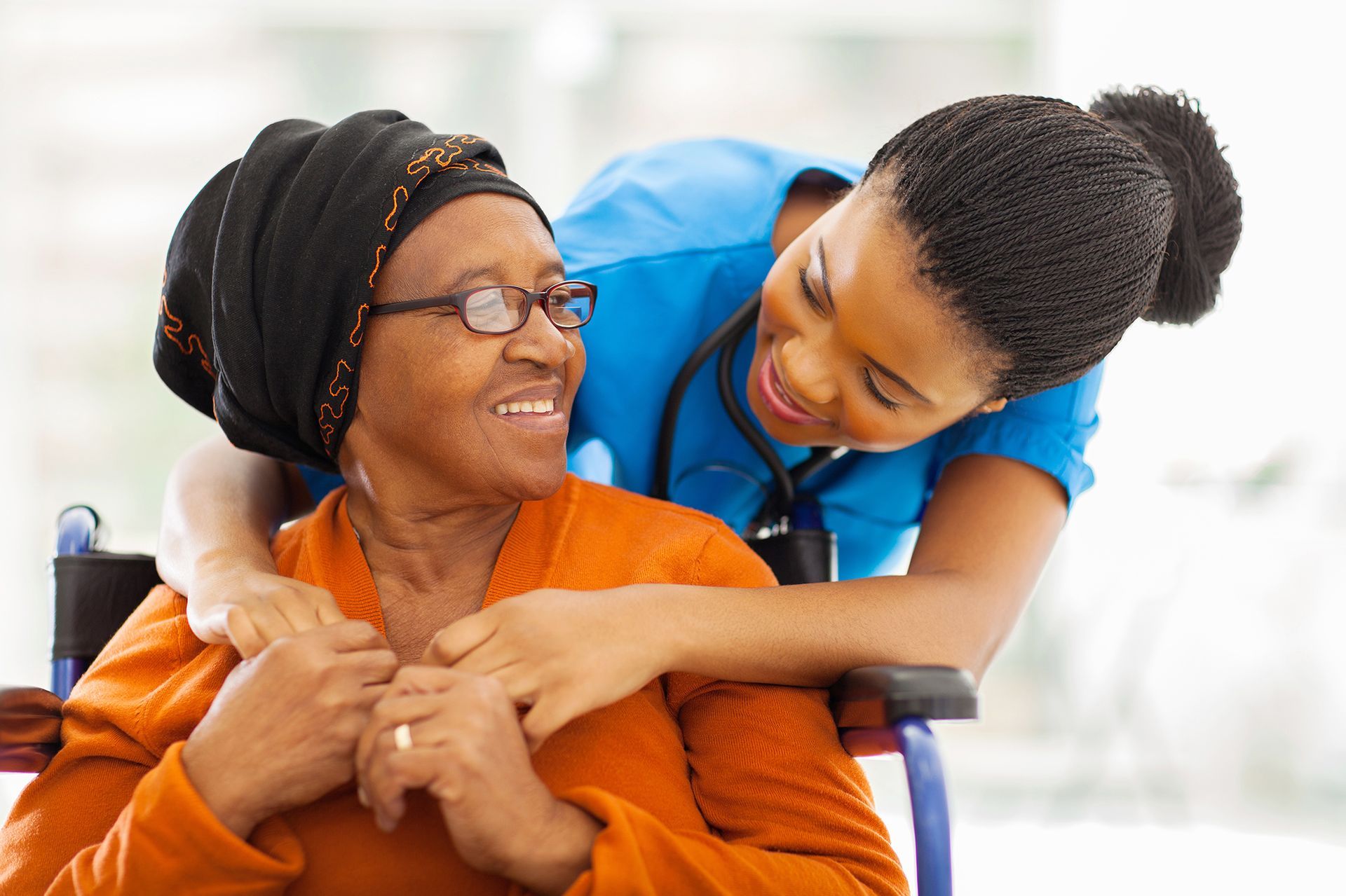 A nurse is hugging an elderly woman in a wheelchair