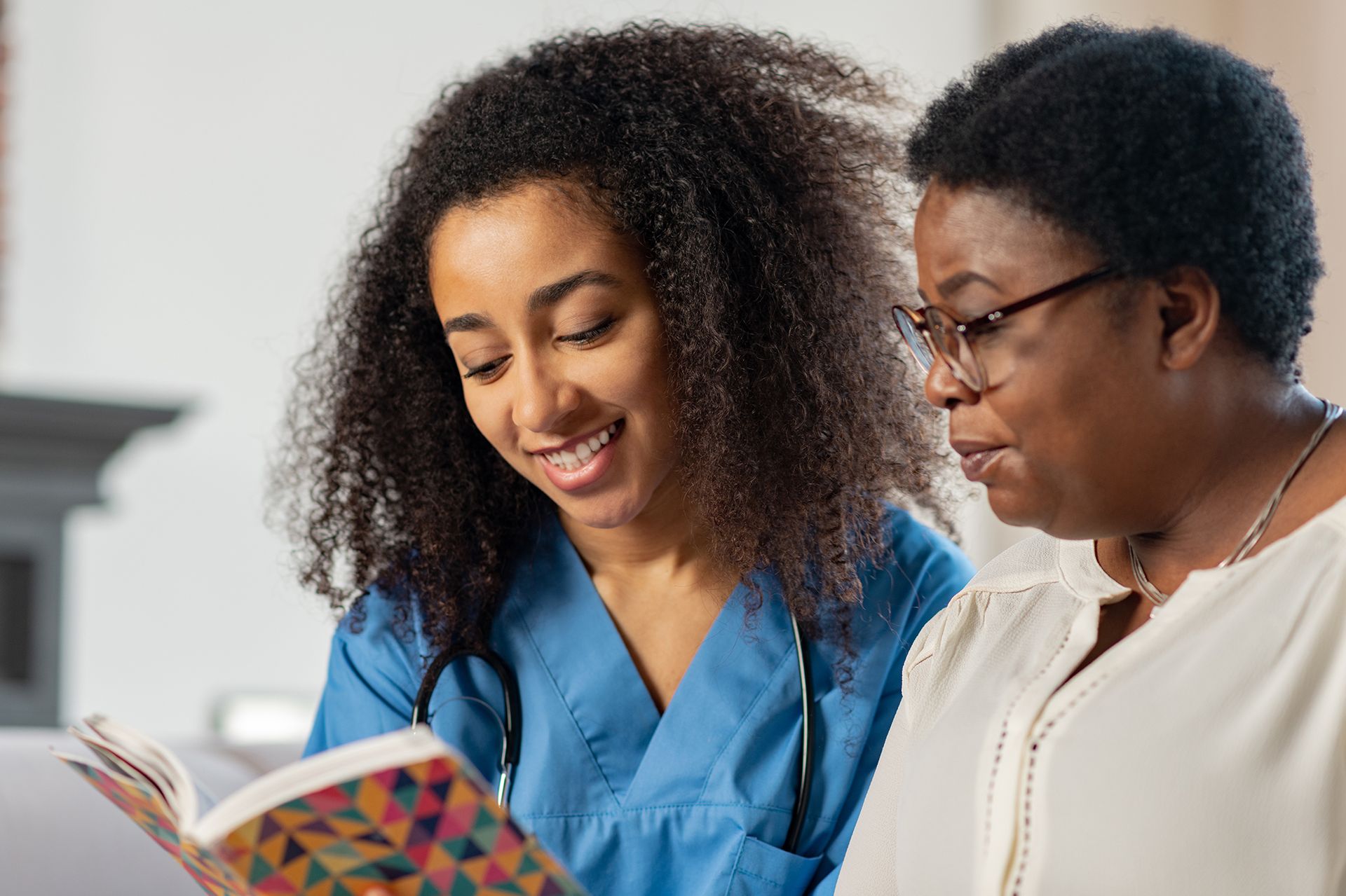 A nurse is reading a book to an older woman