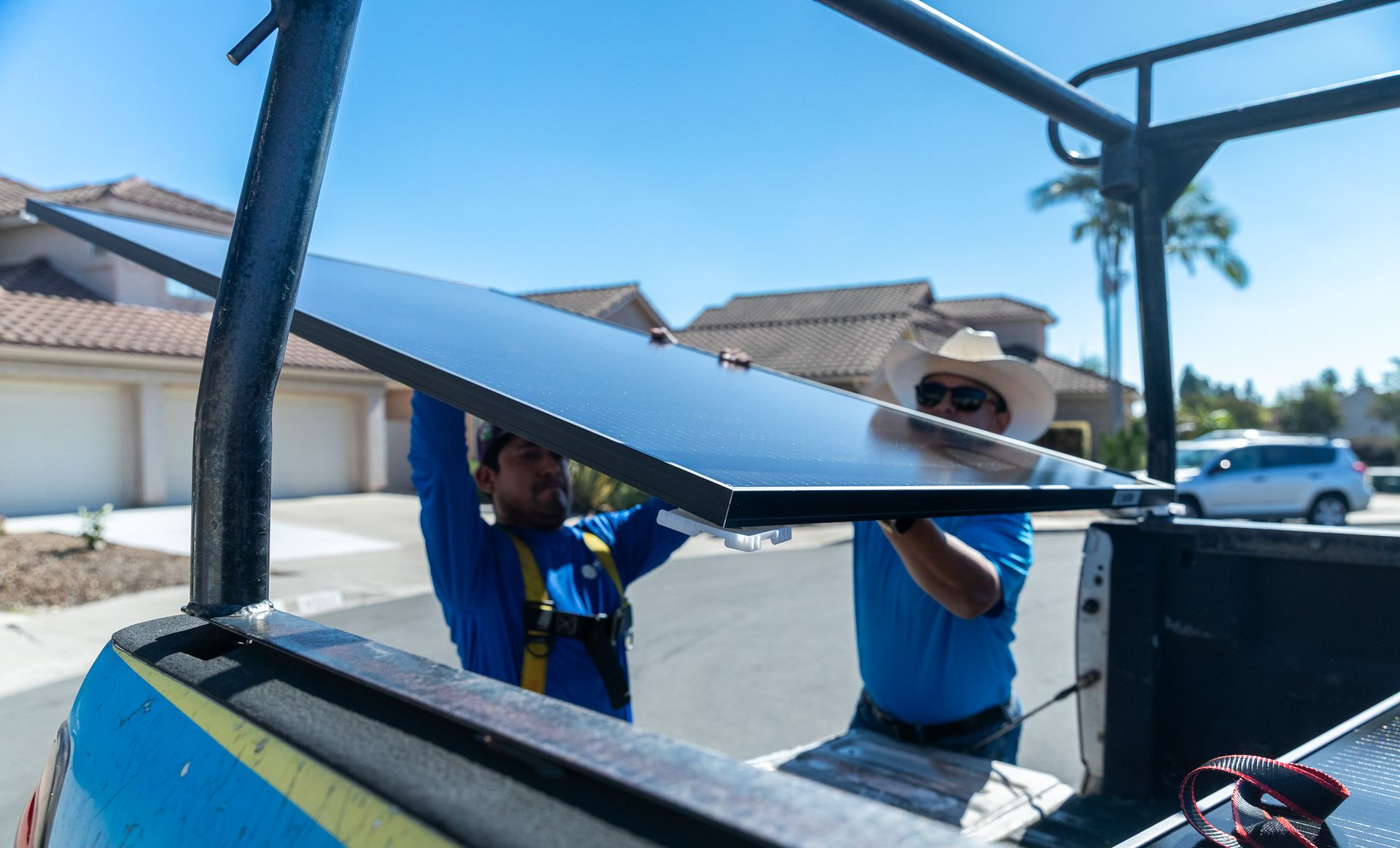 Two people unloading solar panel from a truck in a residential area.
