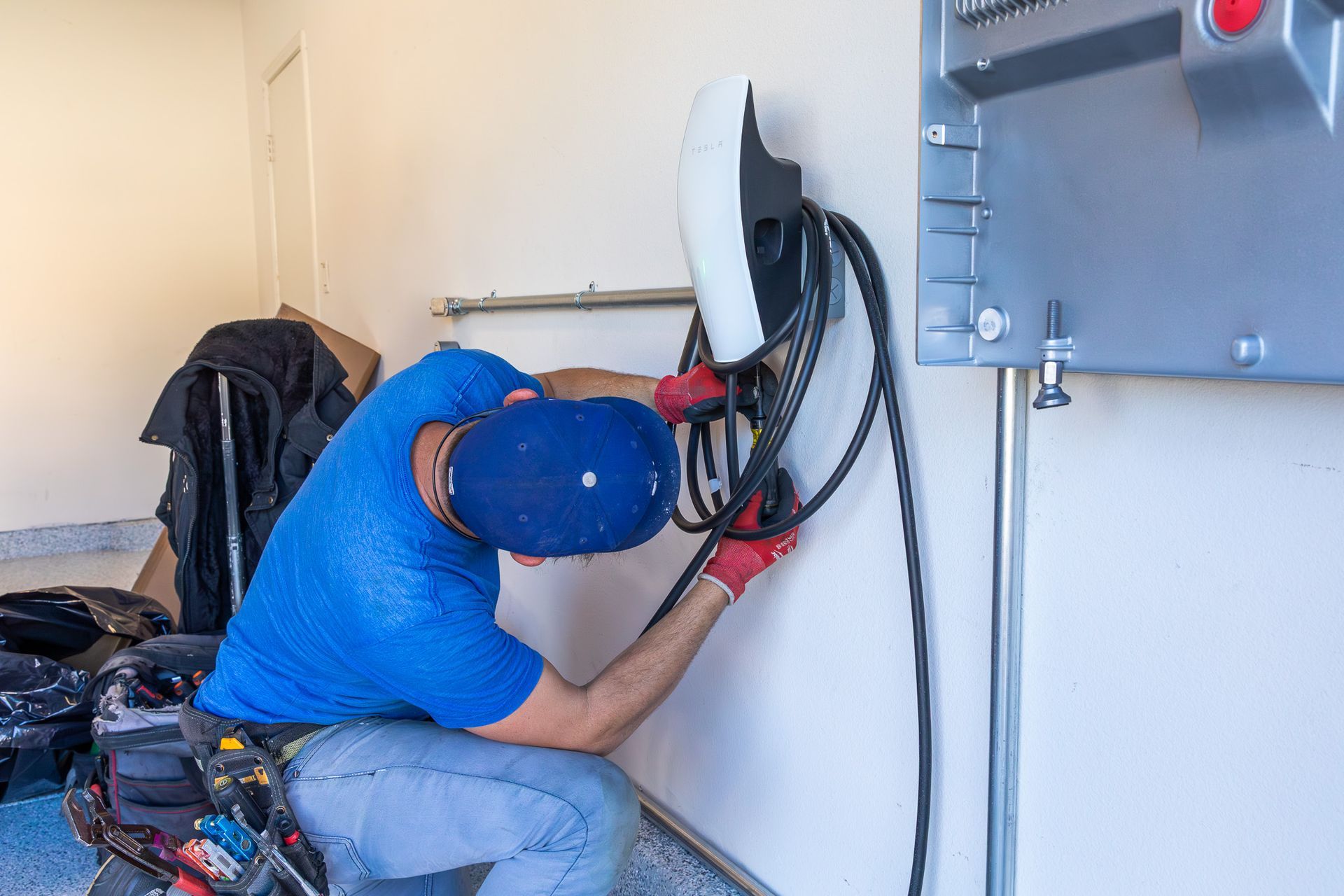 Technician in blue shirt repairing wall-mounted electrical panel with exposed wires