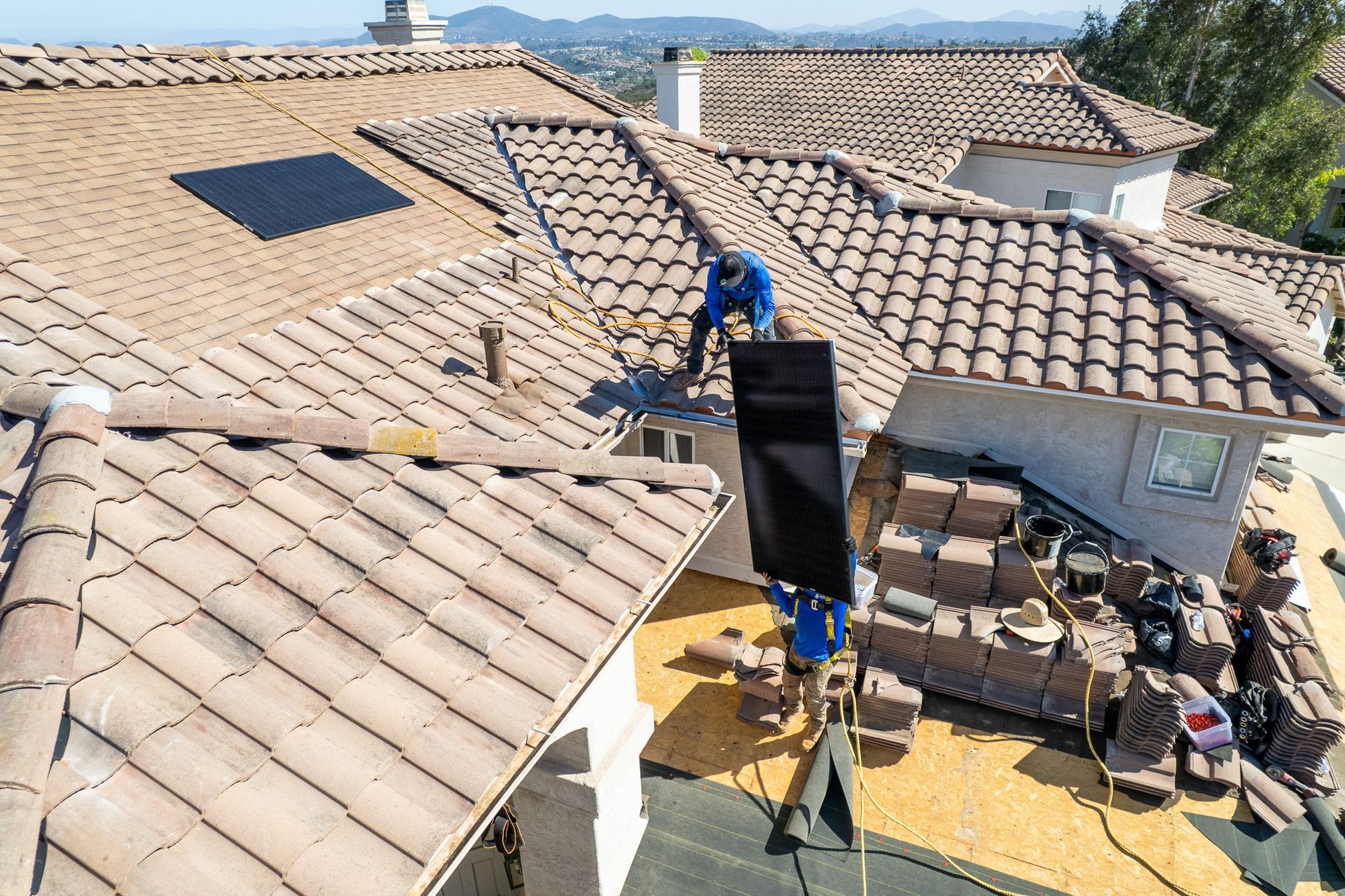 Worker on a tiled roof installing solar panels on a sunny house roof
