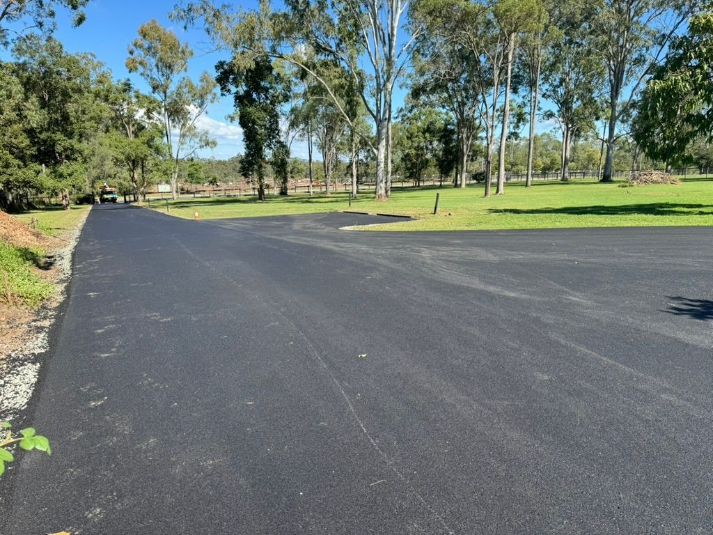 Newly Paved Asphalt Road Curves Through a Grassy Area — Asphalt & Concreting Services & Solutions in Logan, QLD
