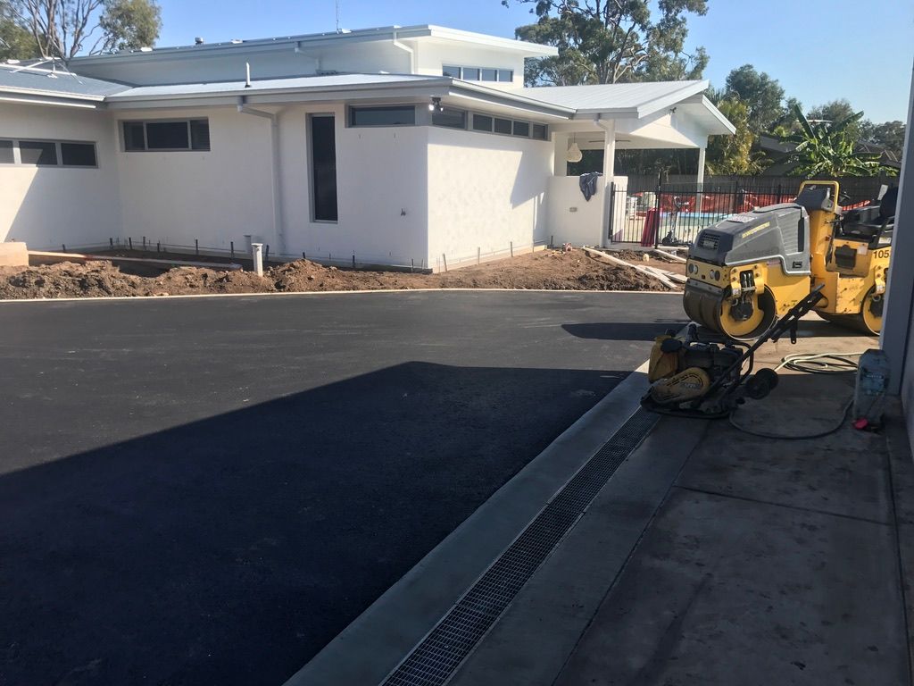 Asphalt Paving With a Small Roller Next to a White Building — Asphalt & Concreting Services & Solutions in Logan, QLD