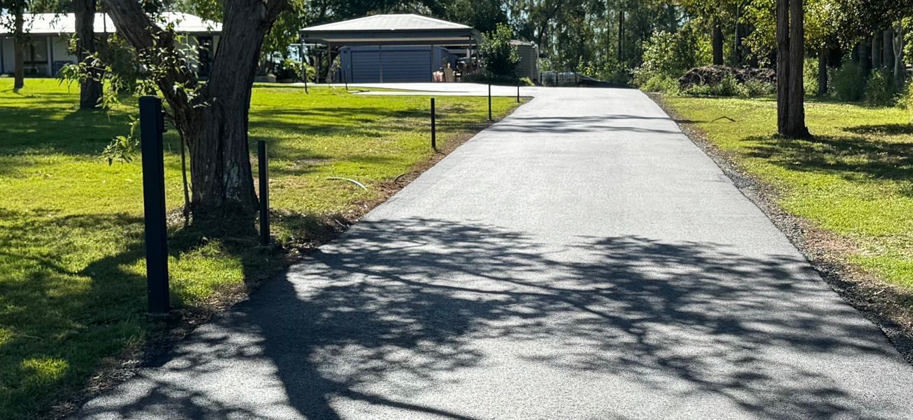 Sunny paved park path leading toward a small pavilion, with trees and grass on both sides.