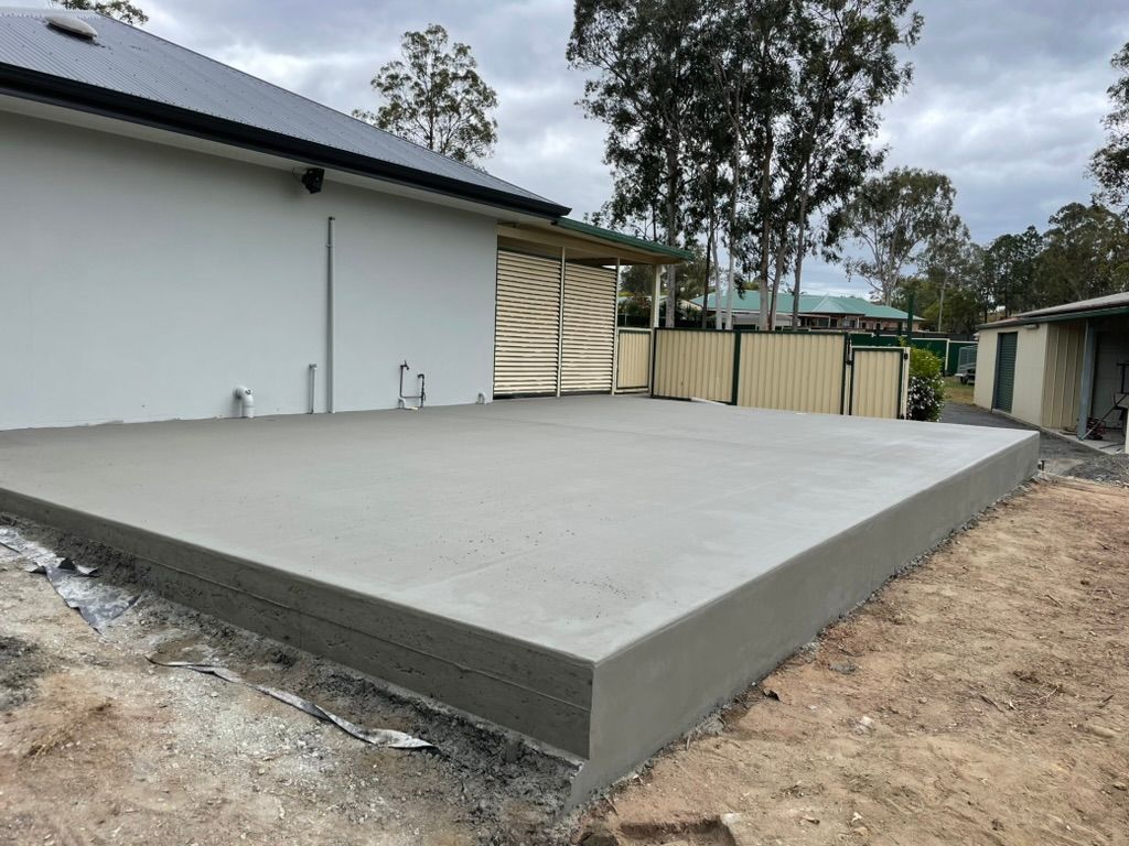 Freshly Poured Concrete Patio Next to a White House — Asphalt & Concreting Services & Solutions in Logan, QLD