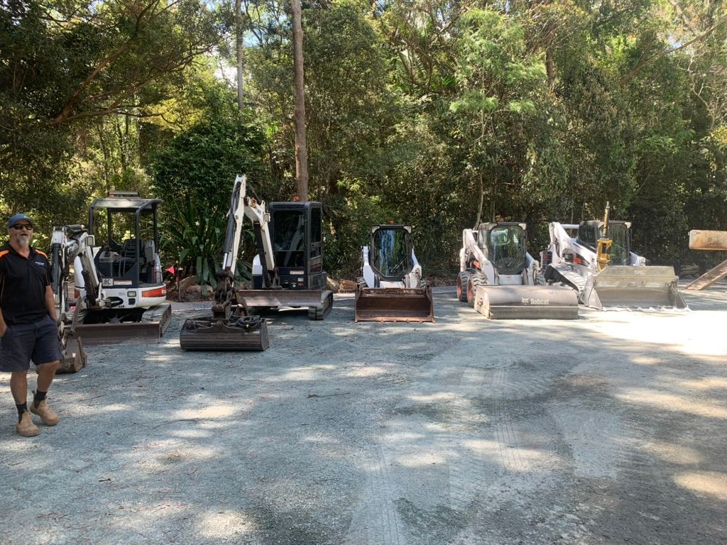 Man Standing by a Row of Small Construction Vehicles — Asphalt & Concreting Services & Solutions in Logan Village, QLD