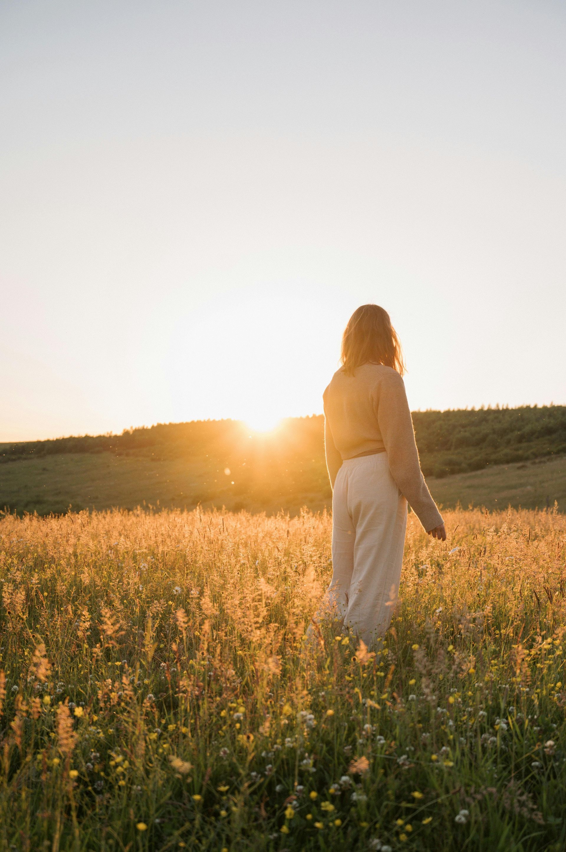 A woman is standing in a field of tall grass at sunset.