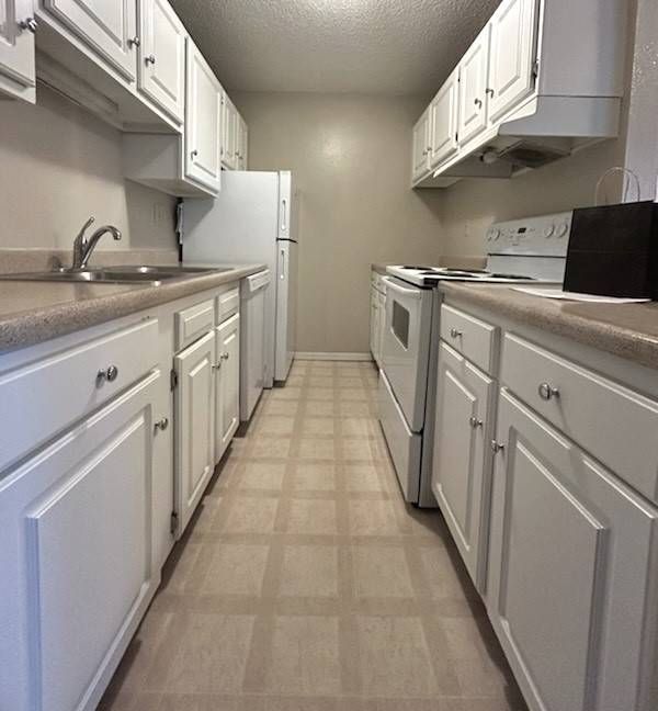 Narrow kitchen with white cabinets, appliances, and beige tile floor.