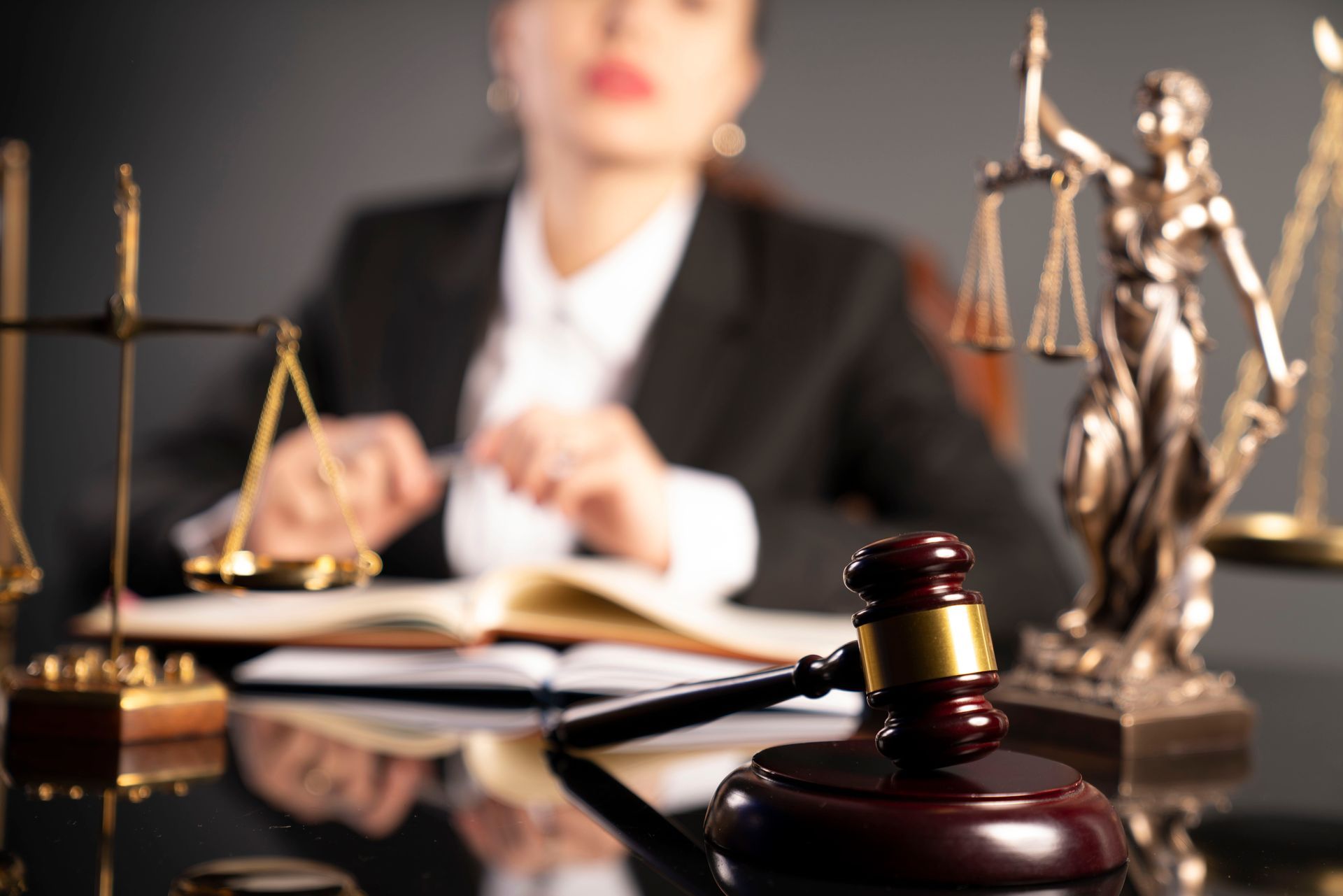 A gavel rests on a desk in front of a blurry legal professional, with scales of justice symbols on both sides.