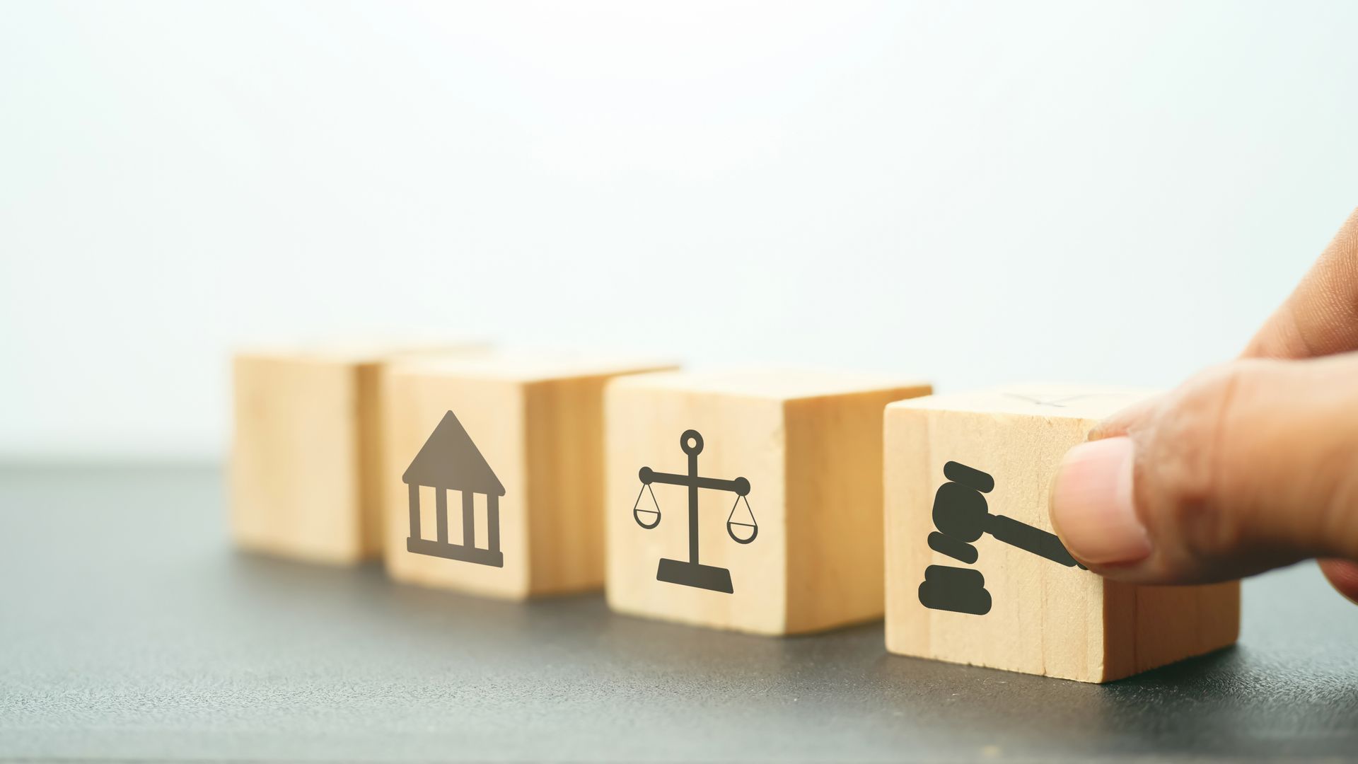Hand arranging wooden blocks with law symbols: courthouse, scales, gavel.