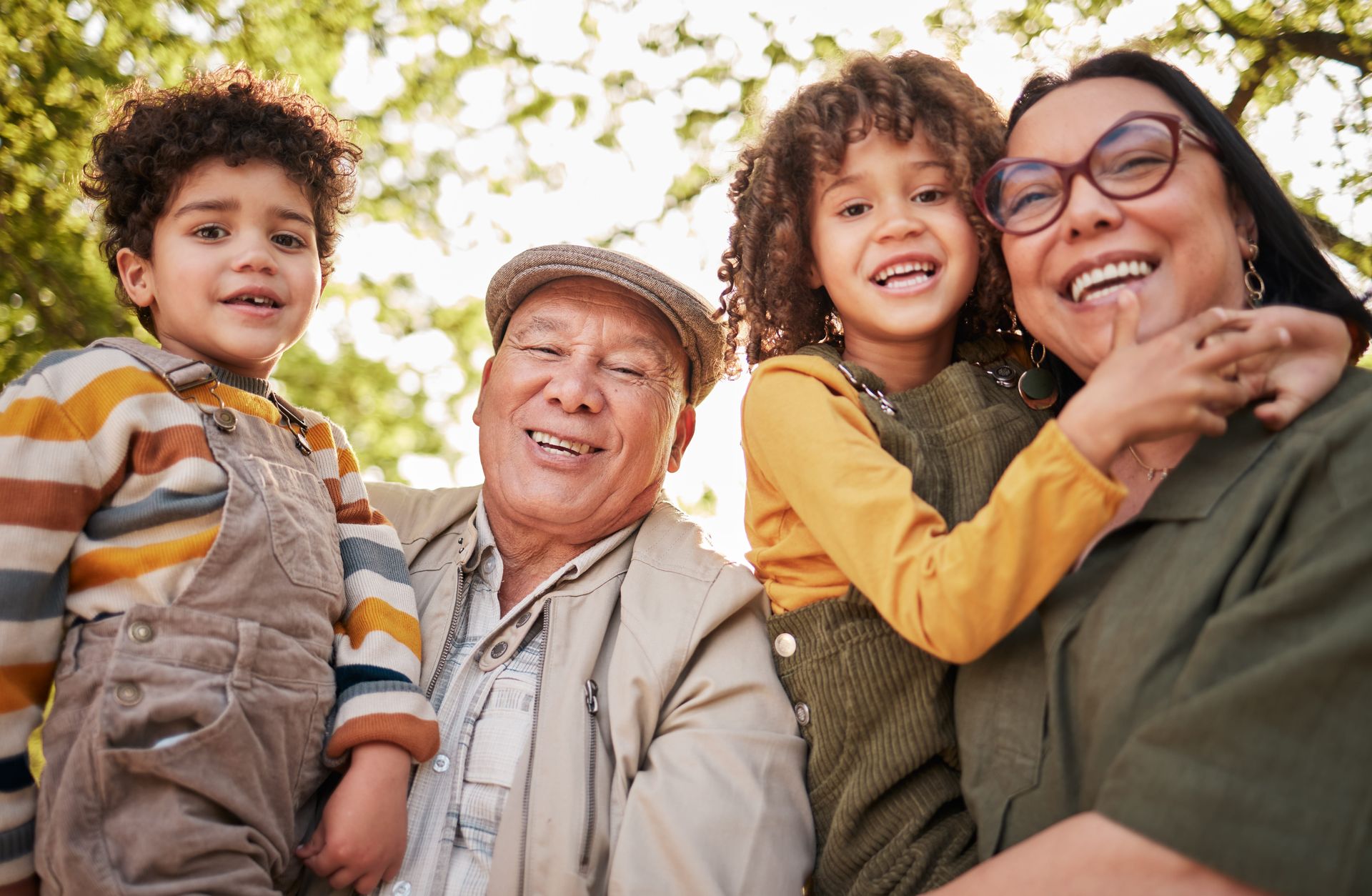A smiling family group of four embracing outdoors in bright natural light.