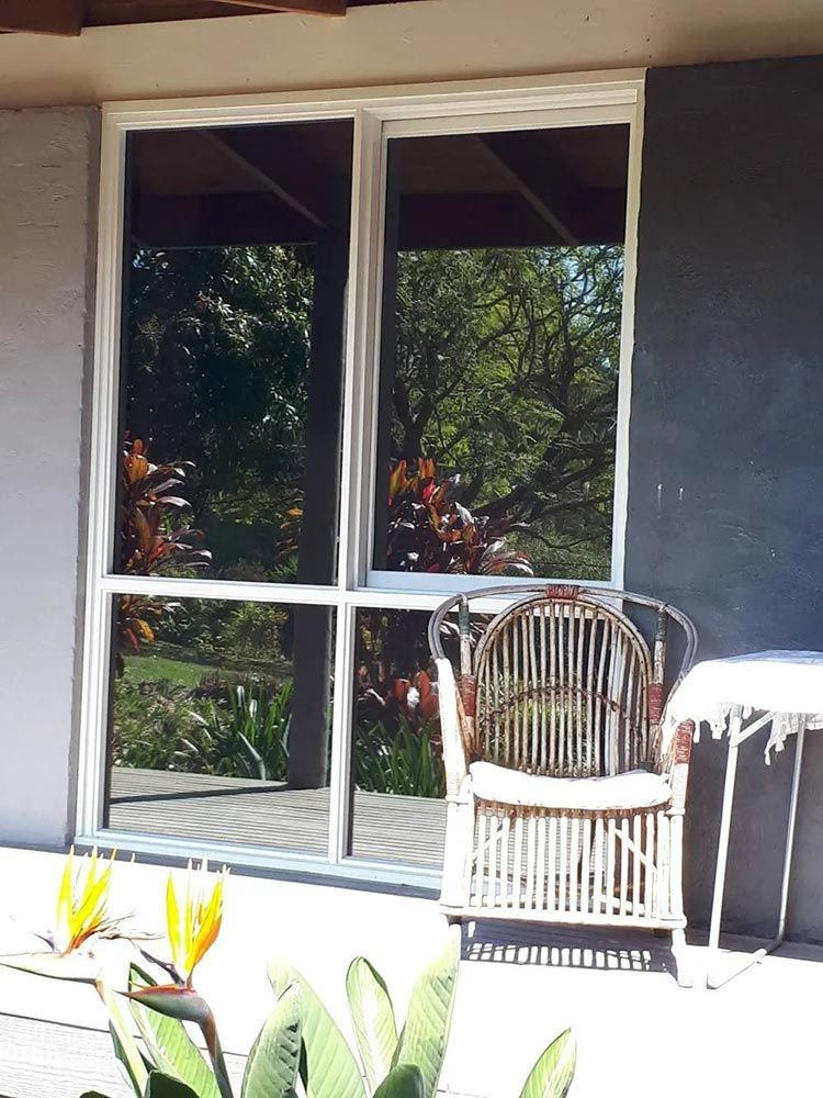 A Wicker Chair Sits in Front of a Large Window — Endrust (Coffs Harbour) in Coffs Harbour, NSW