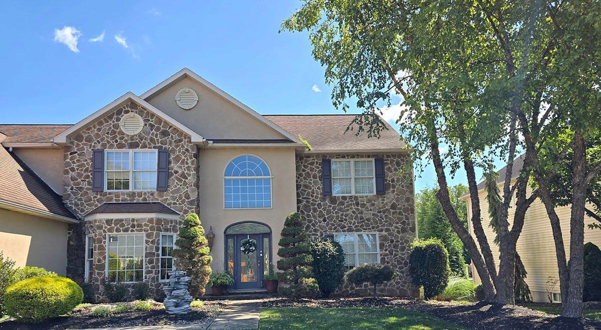 Two-story house with stone facade, arched window, and lush landscaping on a sunny day.